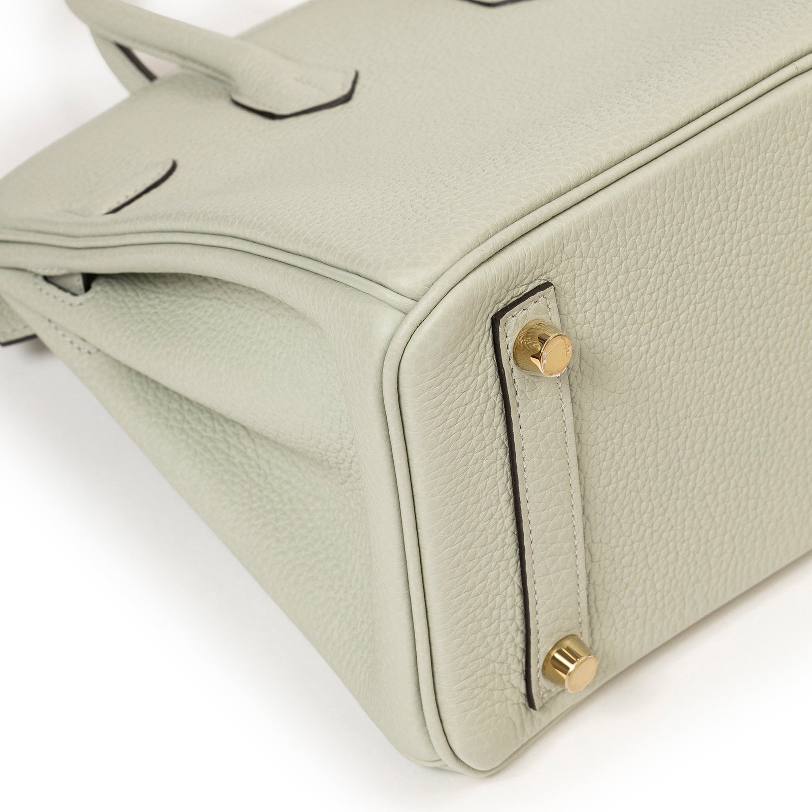 Close-up angled view of textured Hermès Birkin 25 Gris Neve Togo Gold Hardware base corner with gold feet