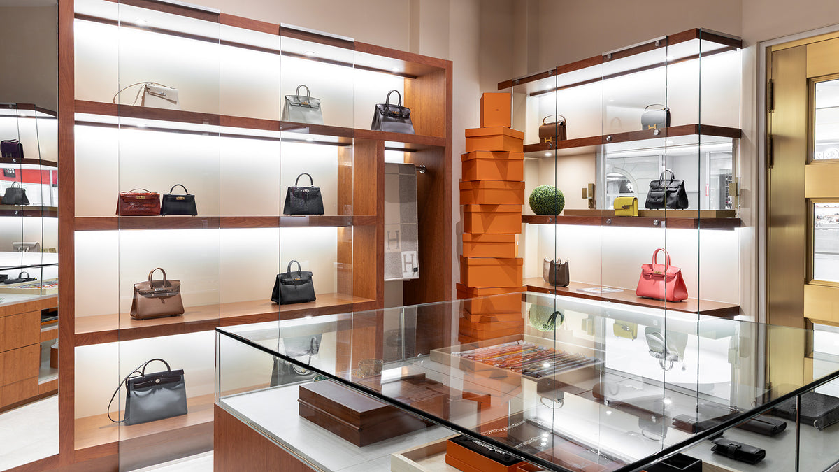 Handbag showroom with glass display cases, illuminated shelves, and stacked orange boxes
