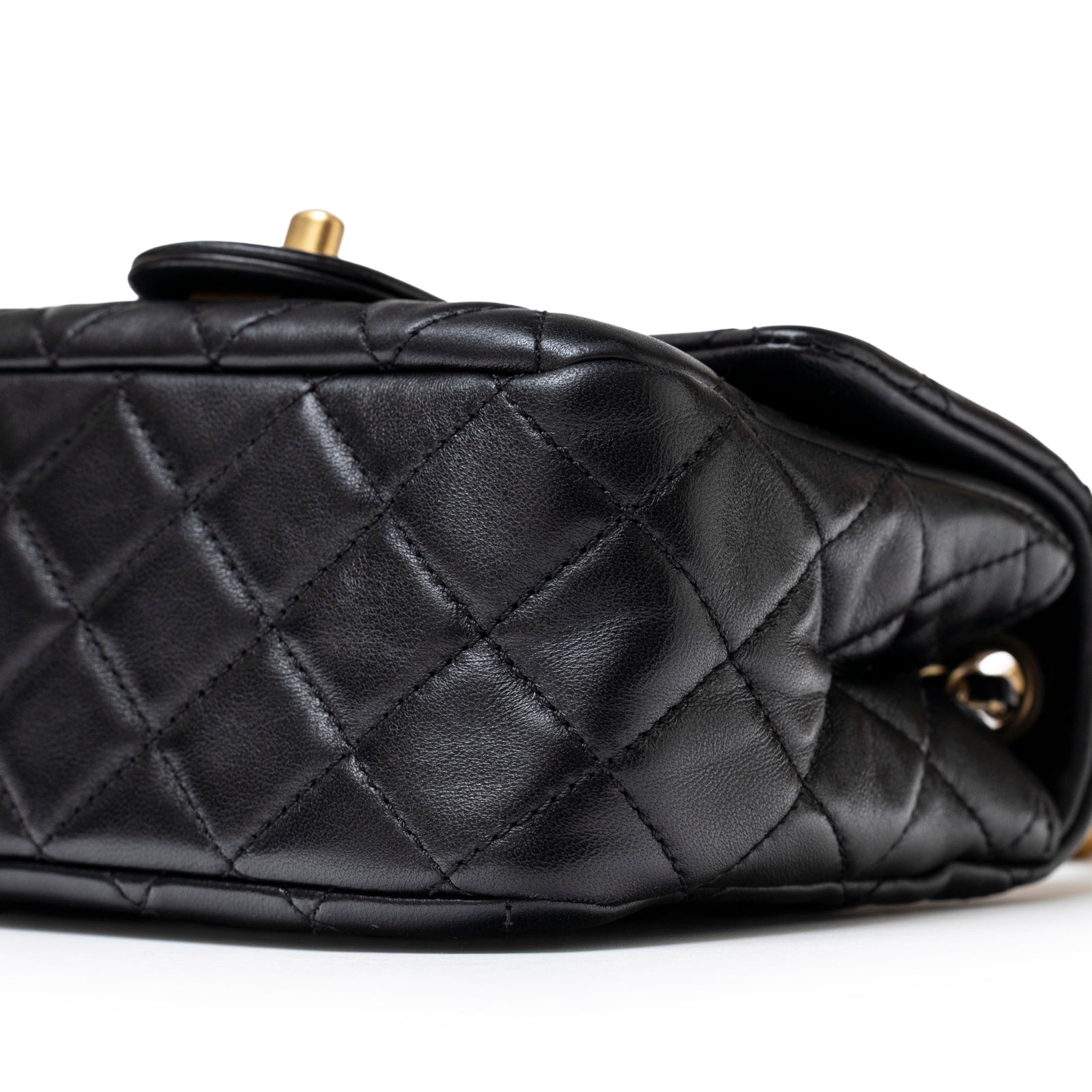 Close-up bottom view of Chanel Mini Square Pearl Crush Flap Bag Black Lambskin Aged Brushed Gold Hardware showing quilting and leather texture