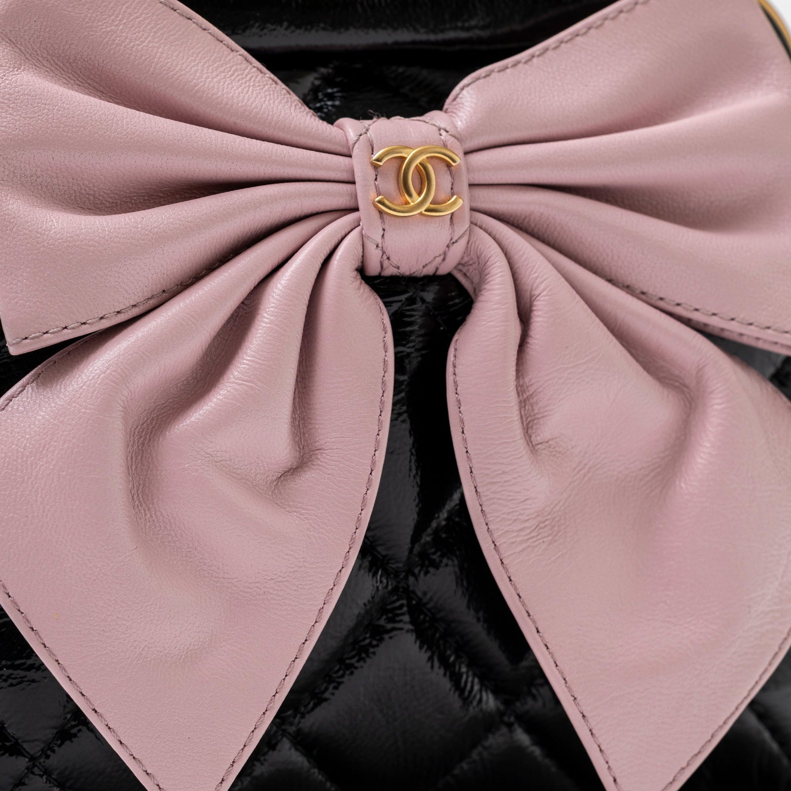 Close-up of pink bow detail with gold logo on Chanel Maxi Bow Clutch With Chain Black/Pink Shiny Quilted Patent Crumpled/Lambskin Brushed Gold Hardware