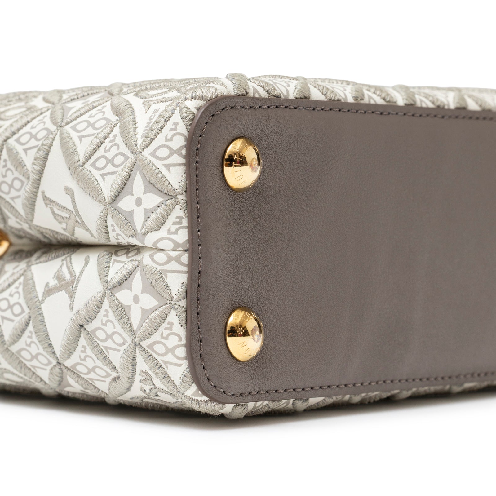 Close-up of base showing gold hardware and embroidered pattern on Louis Vuitton Since 1854 Embroidered Capucines BB Ecru/Taupe Calf Gold Hardware