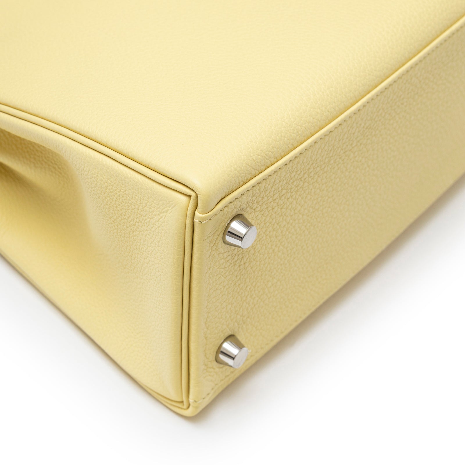 Close-up of bottom corner on Hermès Kelly 25 Retourne Togo Jaune Poussin Palladium Hardware showing leather texture and hardware feet