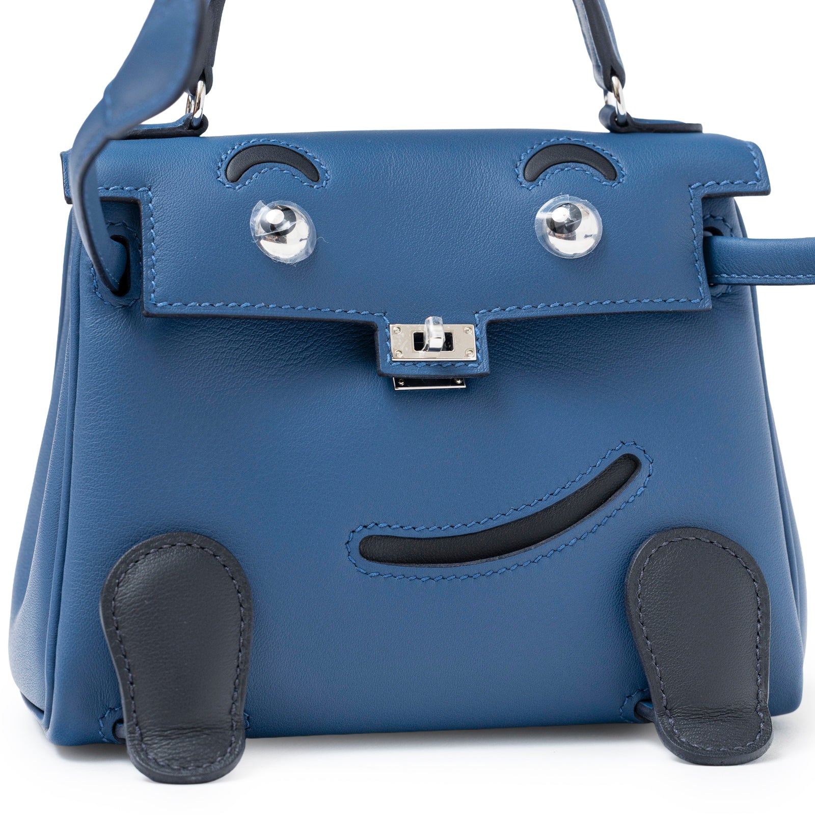 Front view of Hermès Quelle Idolle Kelly Doll Bleu Tie and Caban Swift Palladium Hardware showing smooth leather and facial design detail