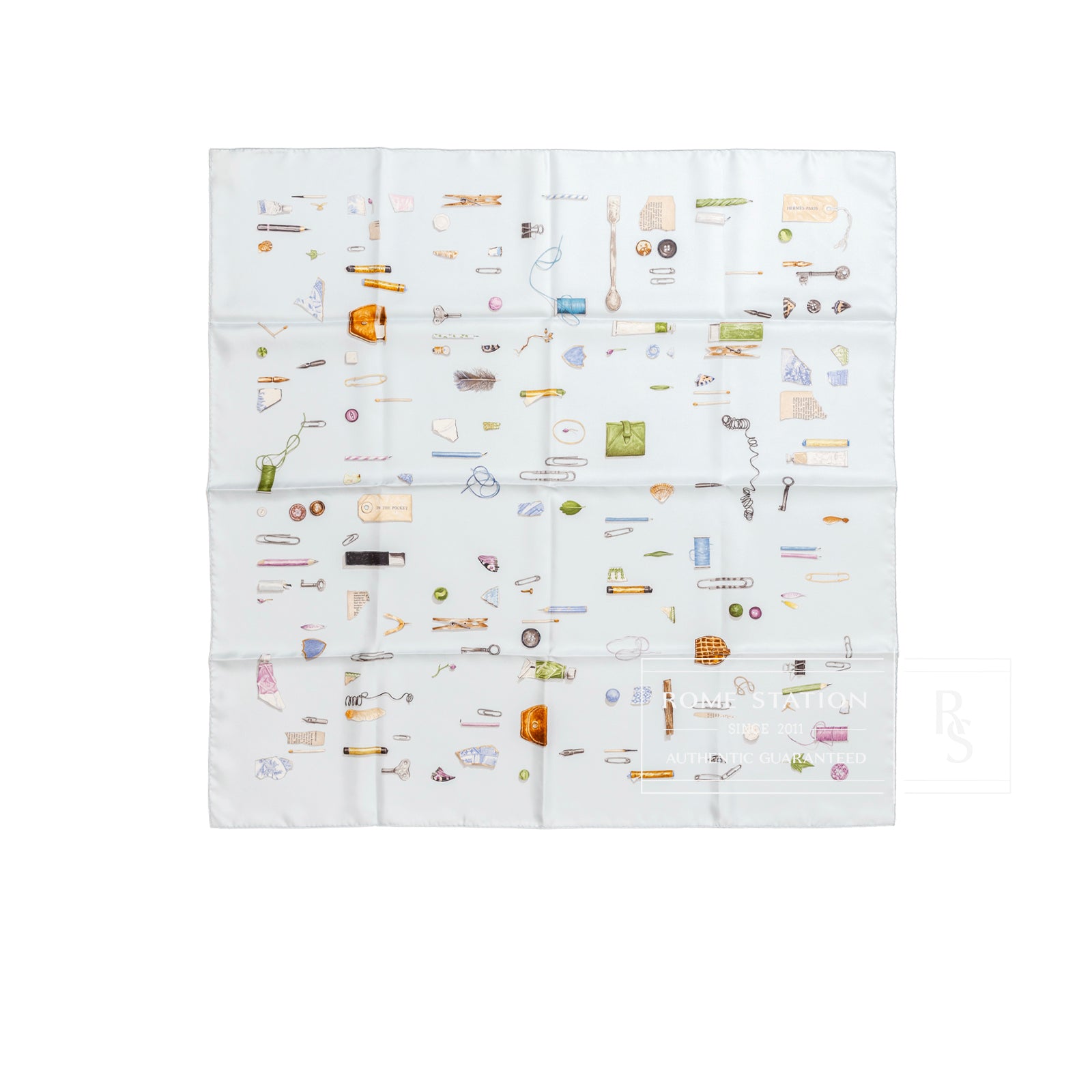 Top-down view of folded Hermès Carre Scarf 90 In The Pocket Blue Glacier/Blue Pale with colorful small illustrations on white background