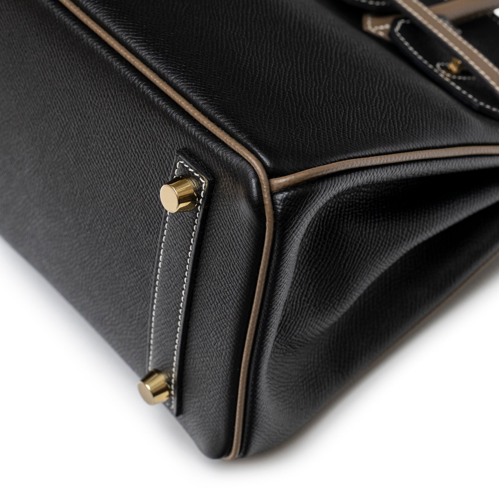 Close-up angled shot of bottom corner showing gold feet and contrasting Etoupe piping on Hermès Special Order HSS Horseshoe Birkin 25 Black/Etoupe Epsom Gold Hardware