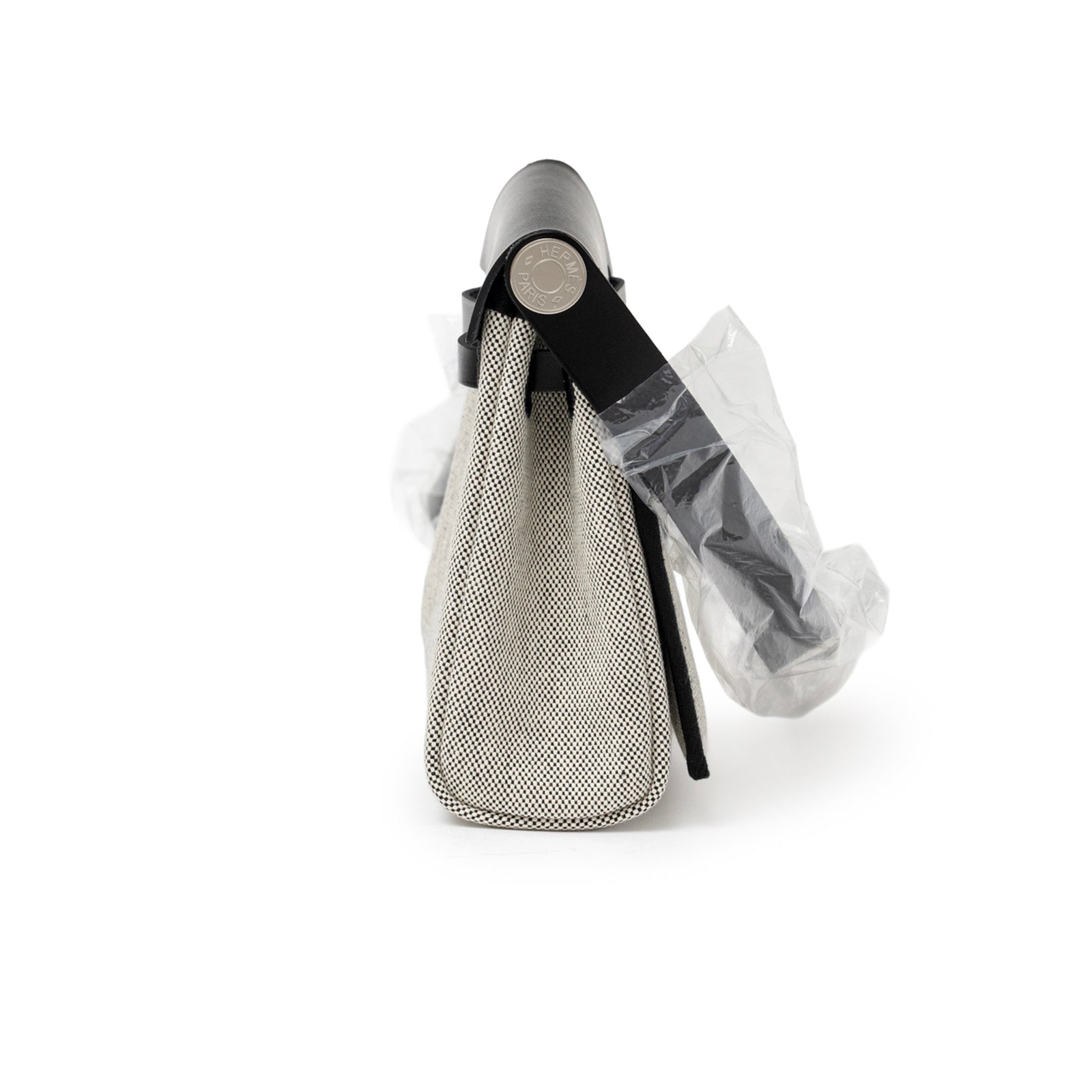 Side view of Hermès Mini Herbag Zip 20 Ecru/Black Toile and Vache Hunter Palladium Hardware with strap wrapped in plastic
