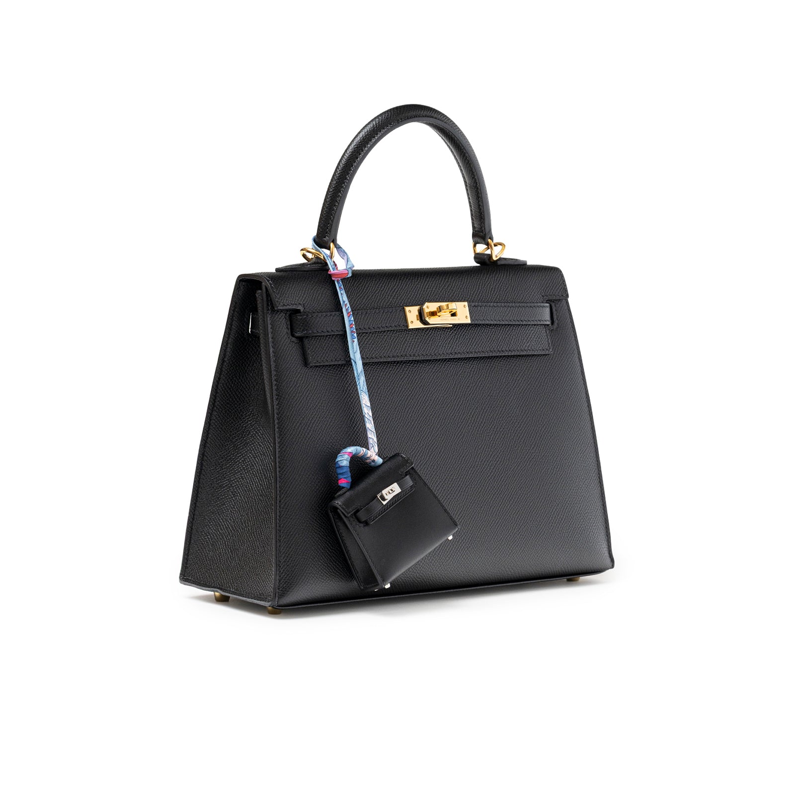 Angled view of Hermès Mini Kelly Twilly Bag Charm Black Tadelakt Palladium Hardware hanging on black leather handbag