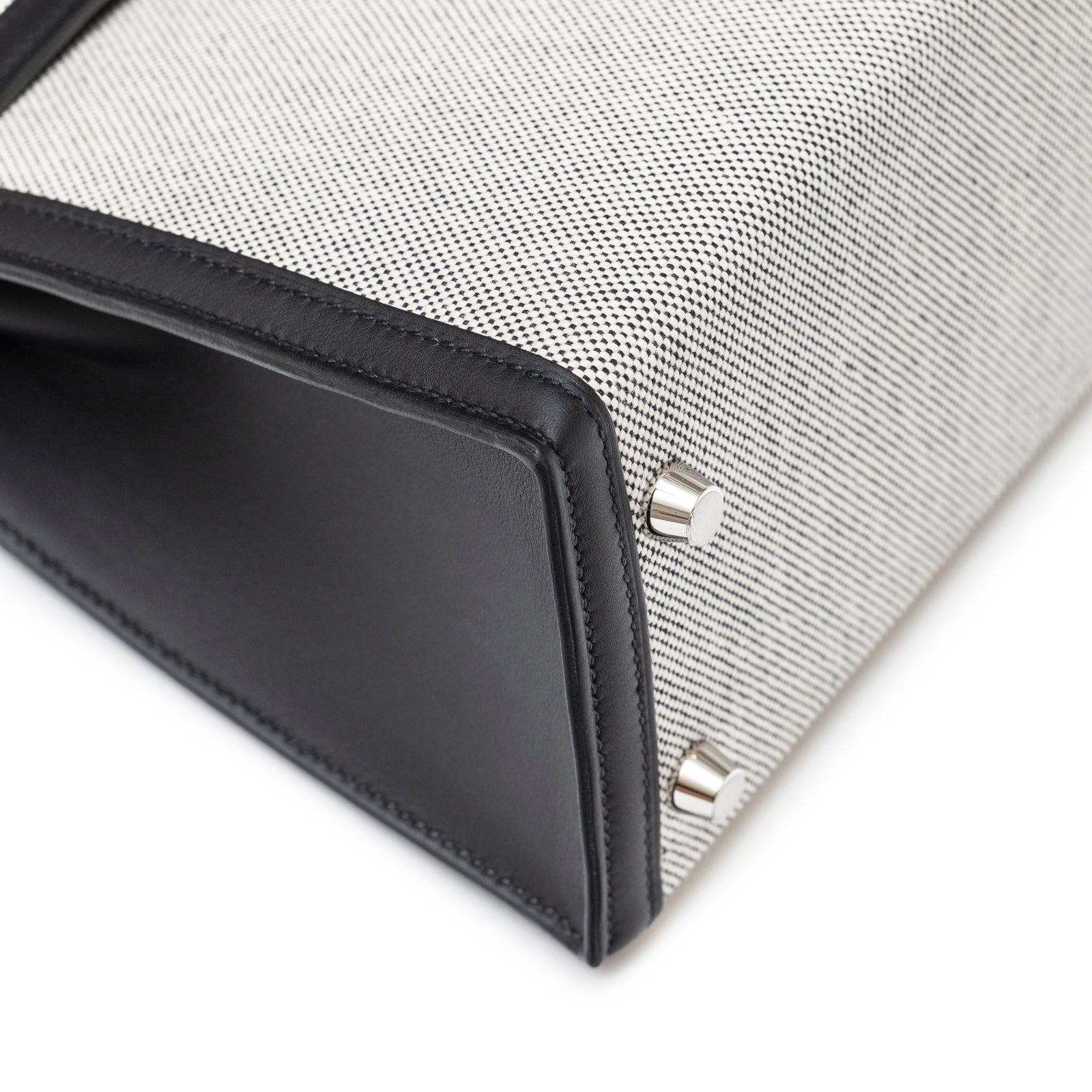 Close-up bottom view of Hermès Kelly 25 Sellier Ecru Black Swift Toile H Canvas Swift Palladium Hardware showing base studs and leather trim