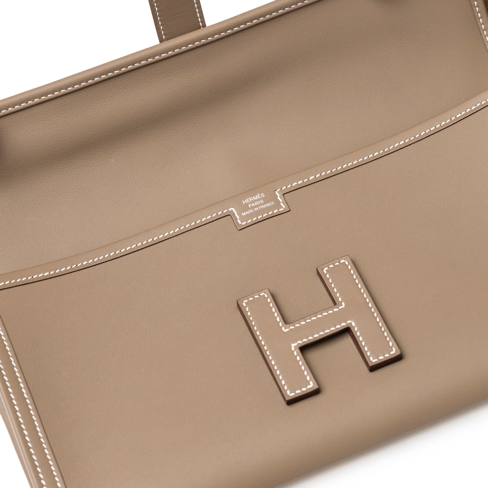 Close-up of Hermès Jige Elan 29 Clutch Etoupe Swift showing detailed white stitching and front "H" clasp in soft taupe leather