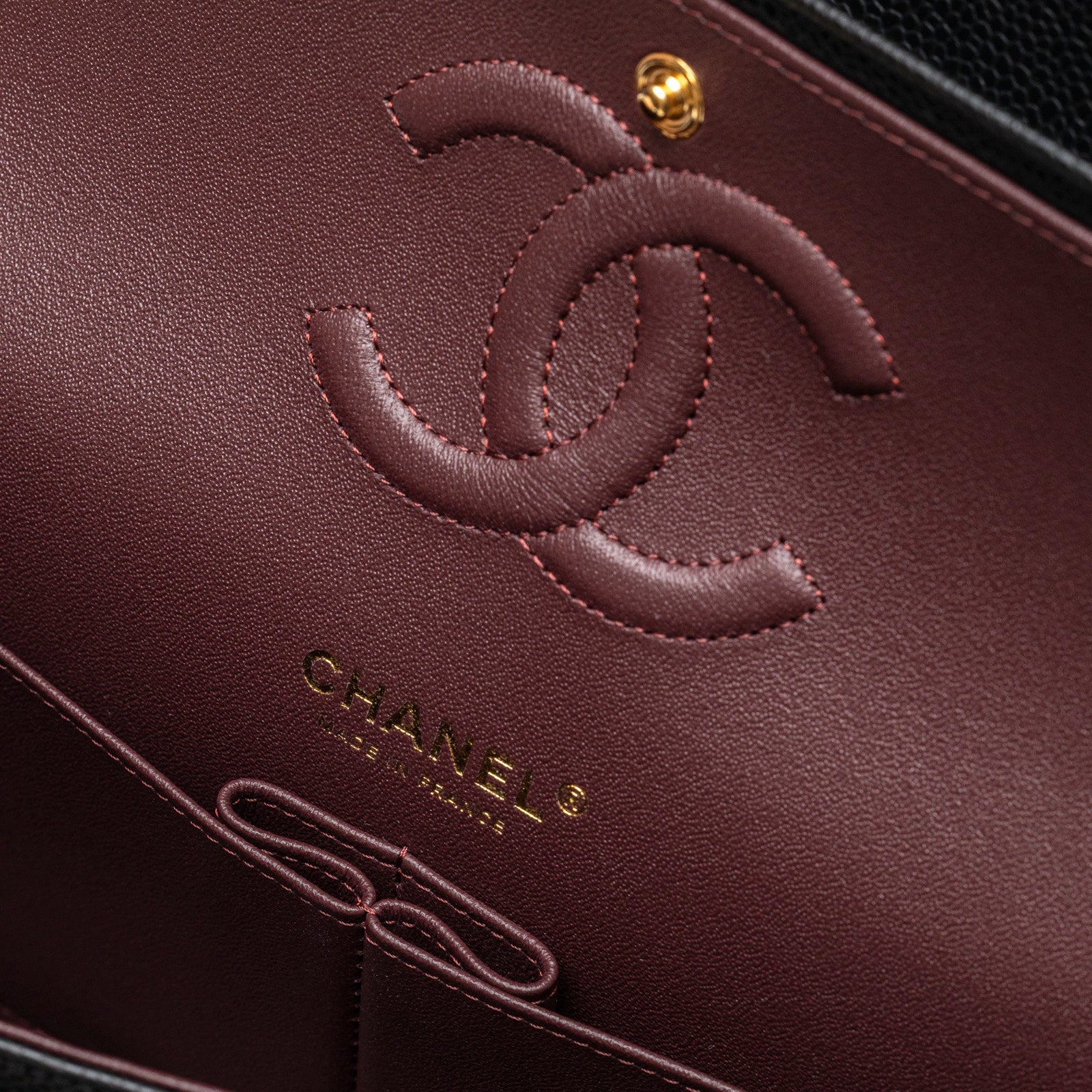 Close-up inside view of Chanel Classic Flap Medium Caviar Black Gold Hardware showing burgundy leather logo and gold stamp