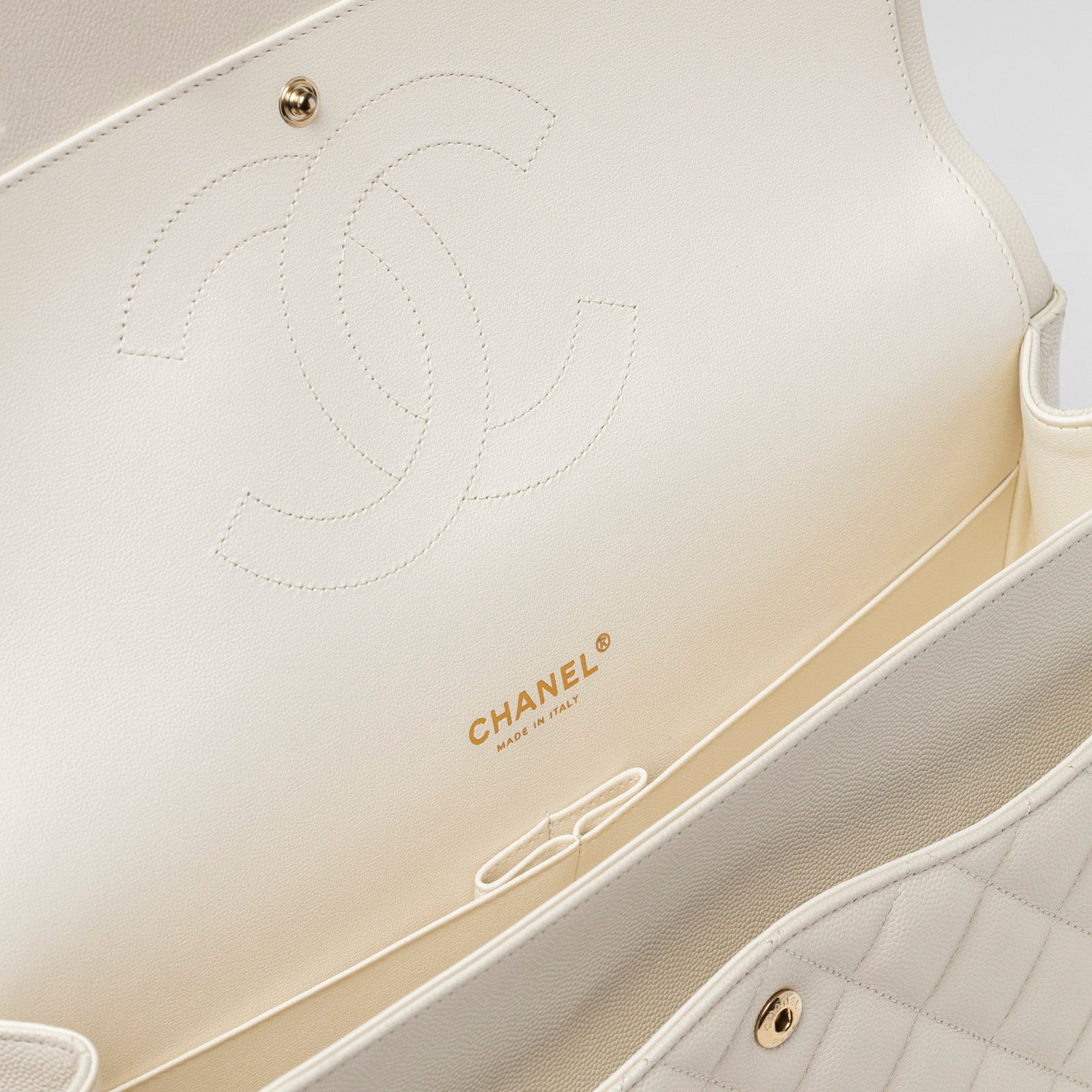 Close-up interior view of Chanel Classic Flap Maxi Caviar White Gold Hardware showing logo embossing and cream leather lining.