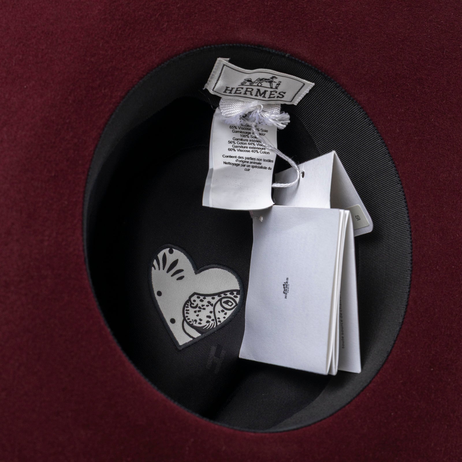 Inside view of Hermès Felt Hat Red Lacquered Brass Heart showing label tags and signature heart detail on burgundy felt lining