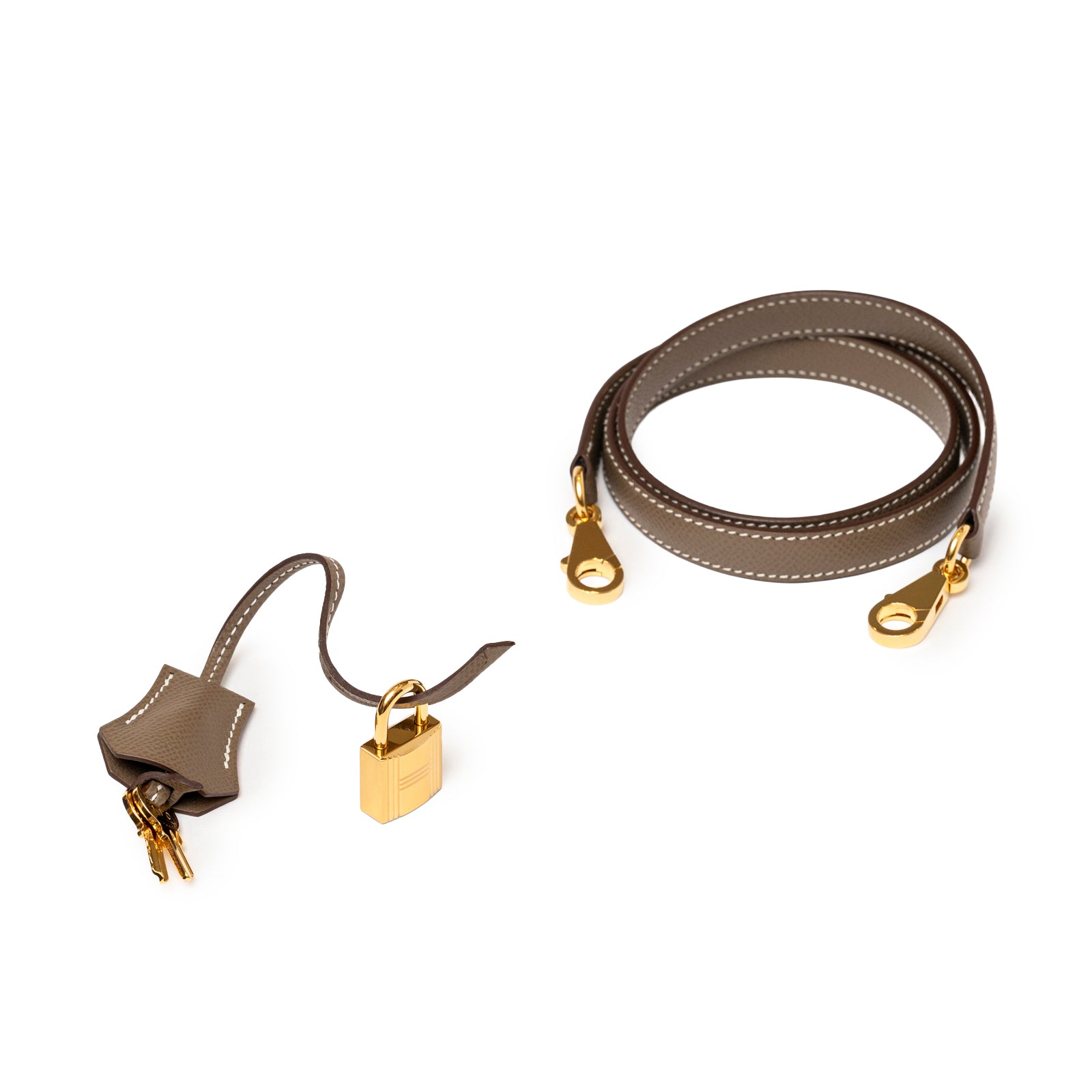 Close-up of Hermès Kelly 28 Sellier Etoupe Epsom Gold hardware strap and gold lock with keys on white background