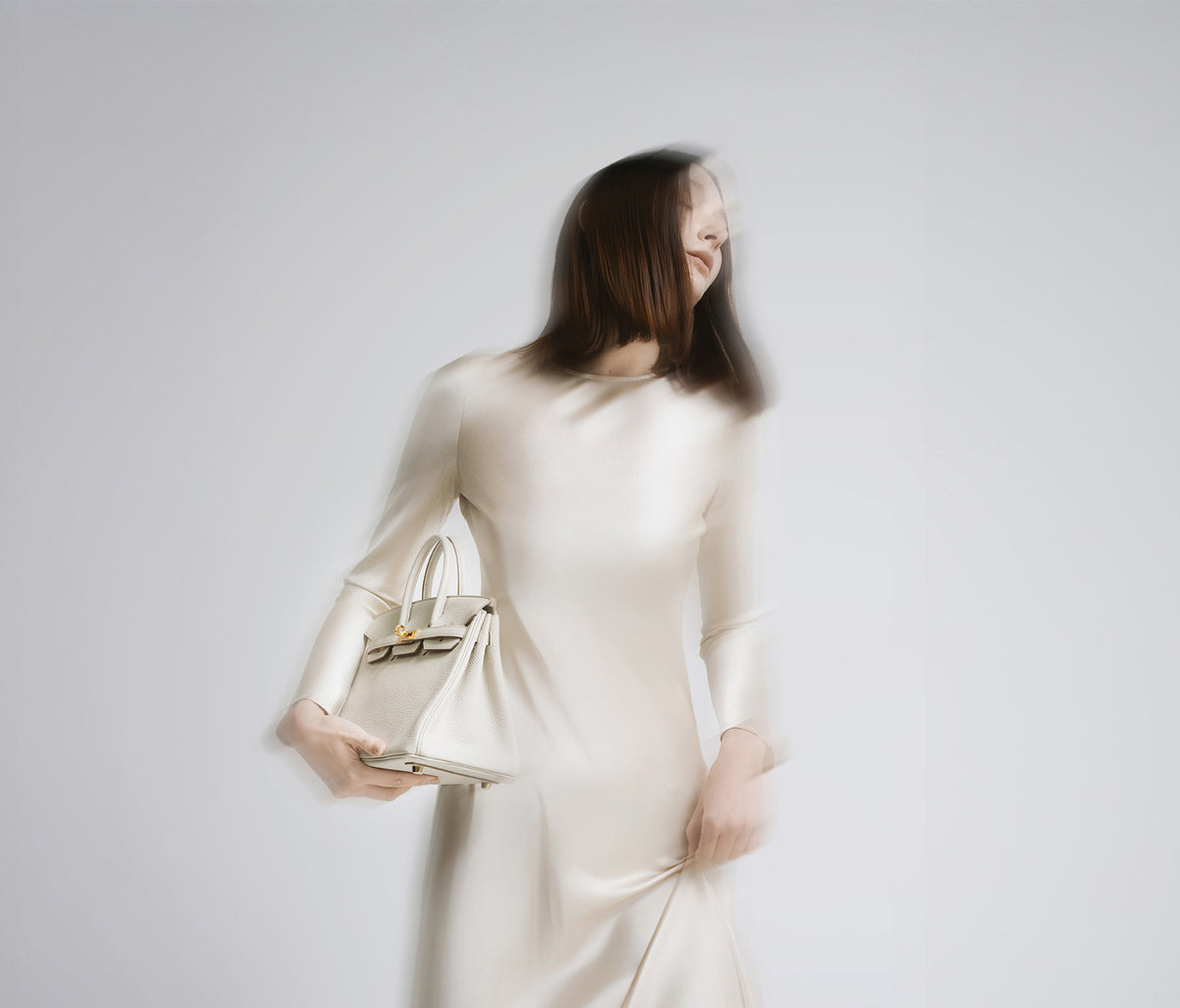 Woman in a cream dress carrying a light Hermès bag