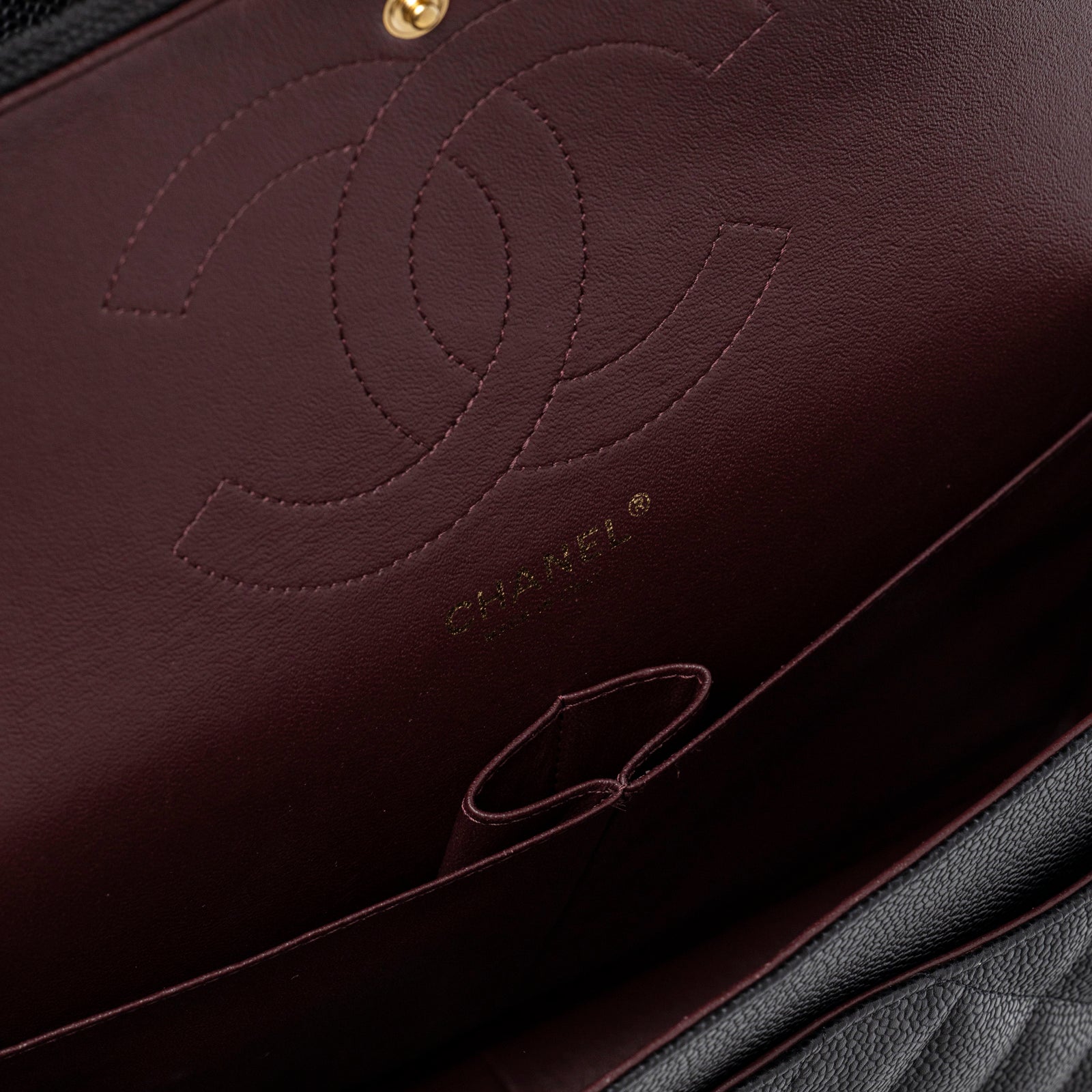 Close-up interior view of Chanel Classic Flap Jumbo Caviar Black Gold Hardware showing burgundy leather lining and embossed logo