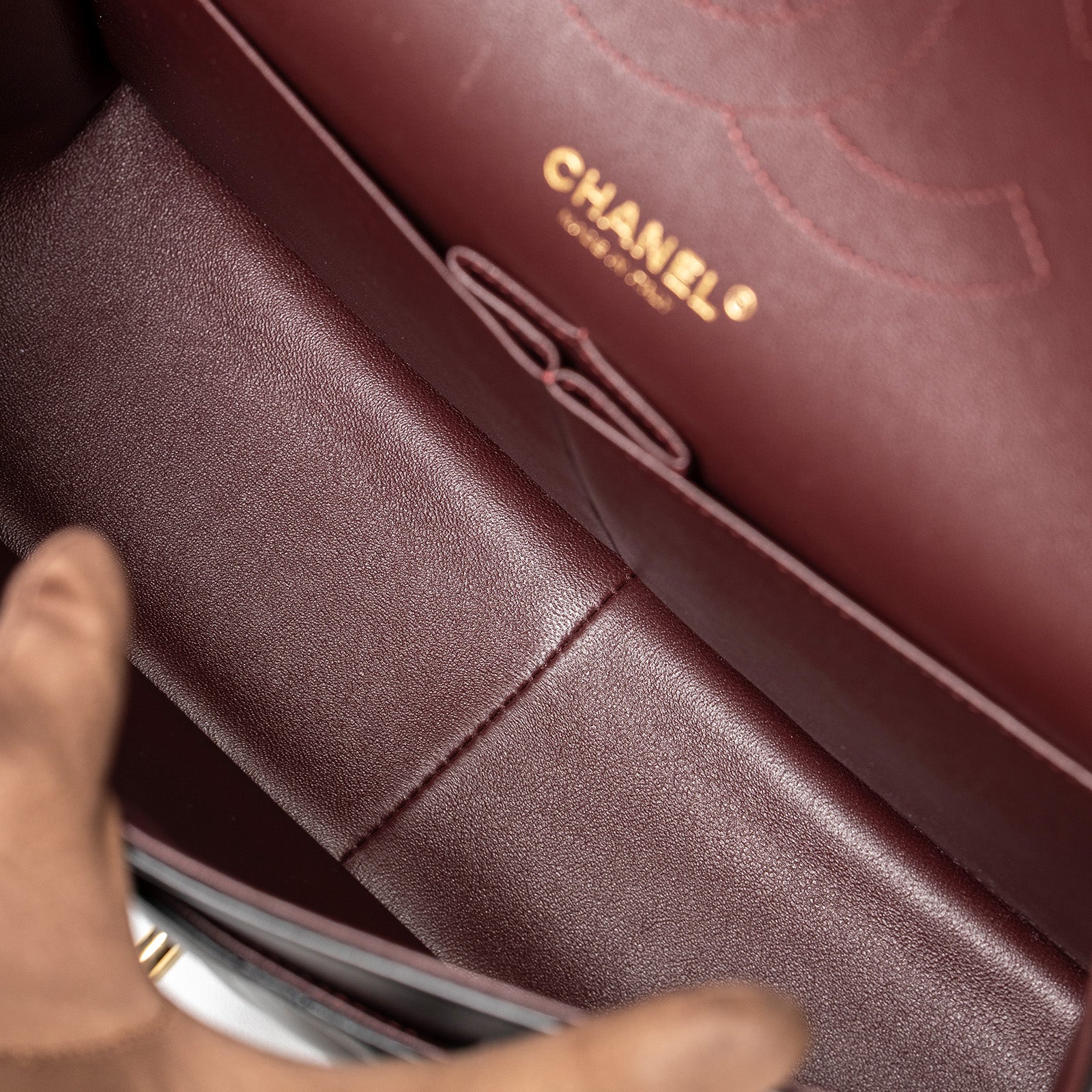 Interior close-up of Chanel Jumbo Classic Double Flap Bag Black Lambskin Gold Hardware showing burgundy leather lining and logo embossing