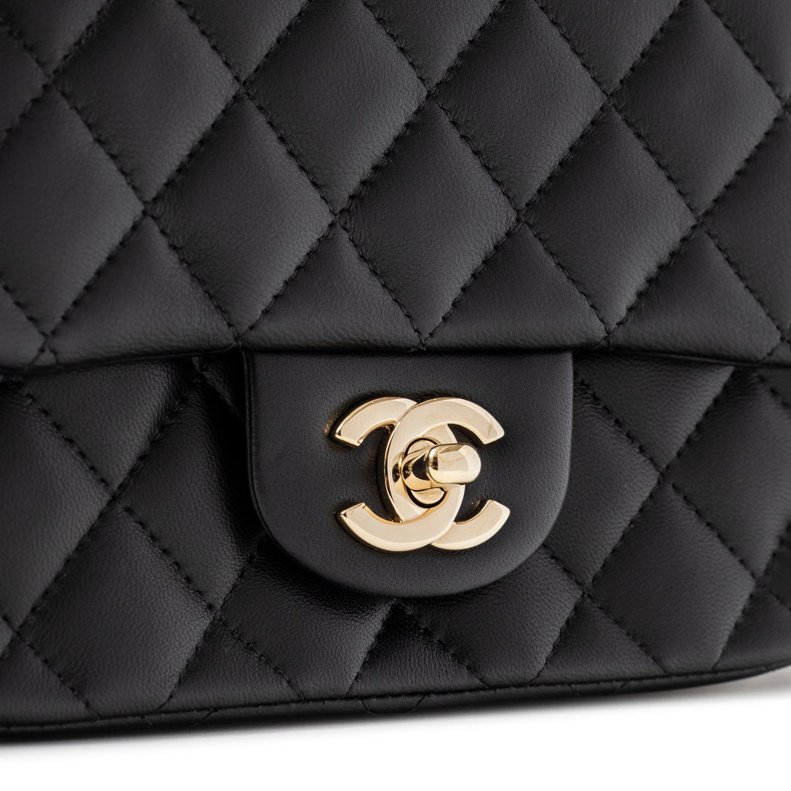 Close-up of gold logo clasp on quilted black lambskin Chanel Mini Square Classic Flap bag Black Lambskin Light Gold Hardware