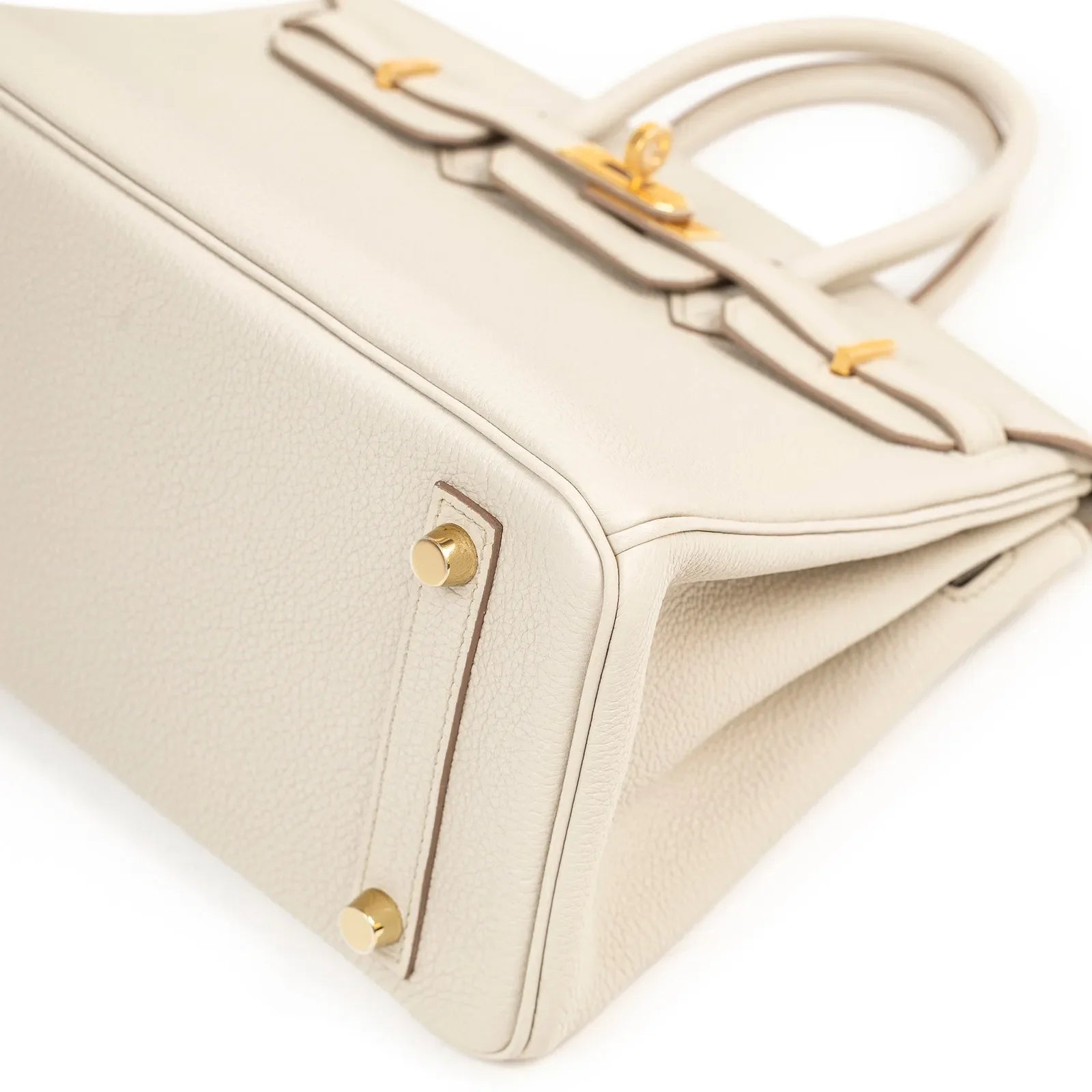 Close-up angled shot of beige togo leather handbag base showing gold hardware feet and fine stitching detail