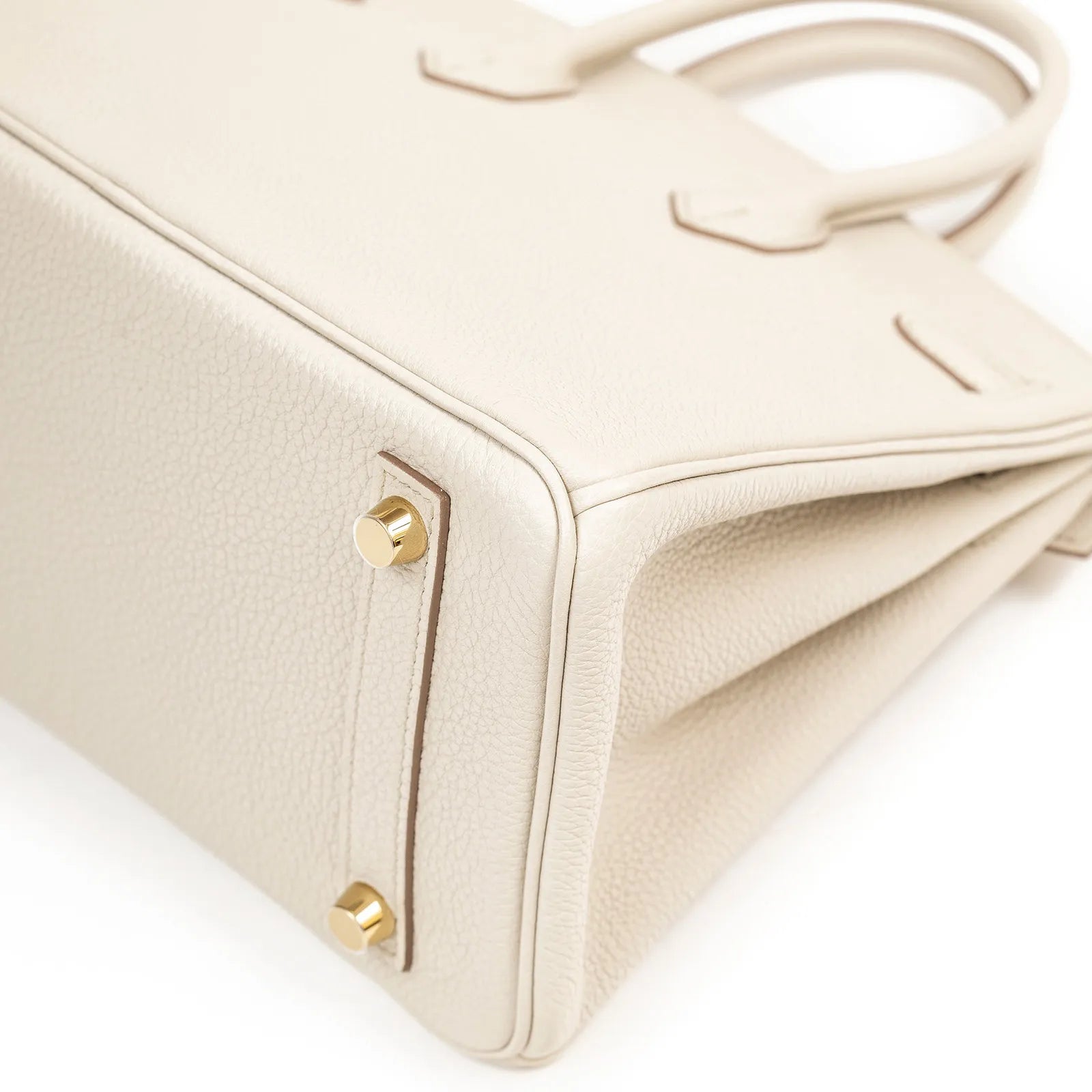 Close-up angled shot of Hermès Birkin 25 Beton Togo leather corner with gold hardware feet and textured finish