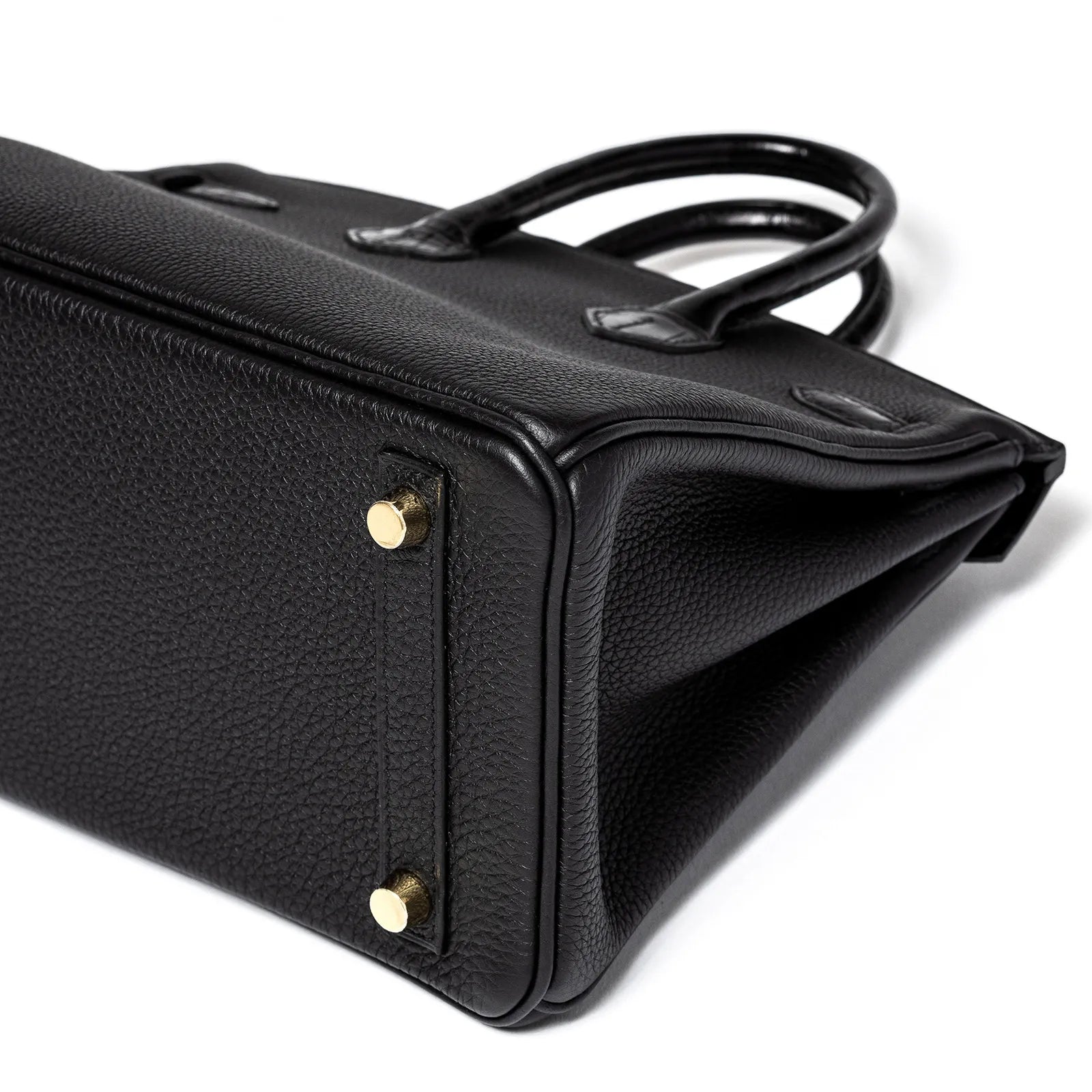 Close-up of the black Togo leather base and gold feet hardware on Hermès Birkin 25 handbag side angled view