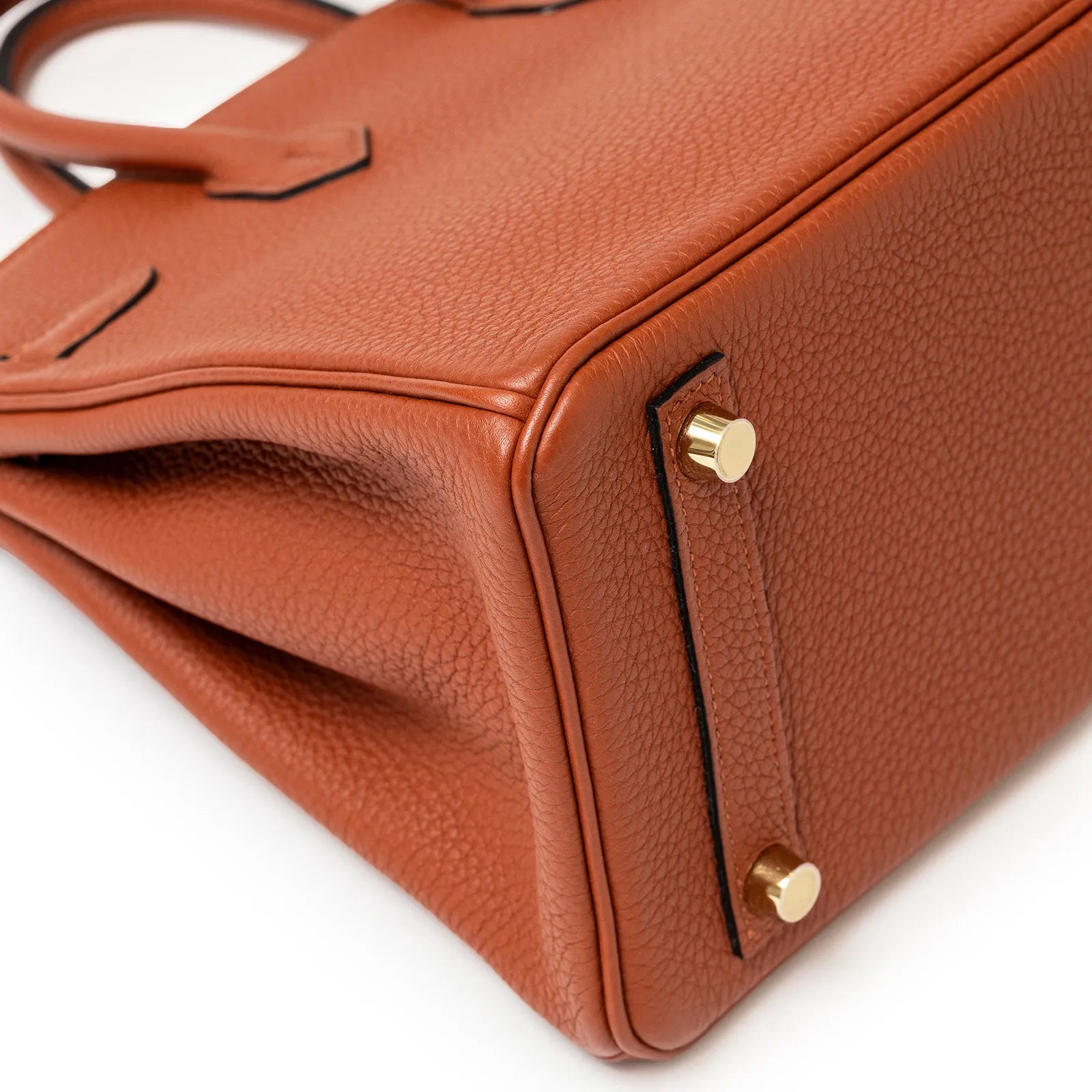 Close-up angled view of copper togo leather bag corner showing gold hardware feet and texture details.