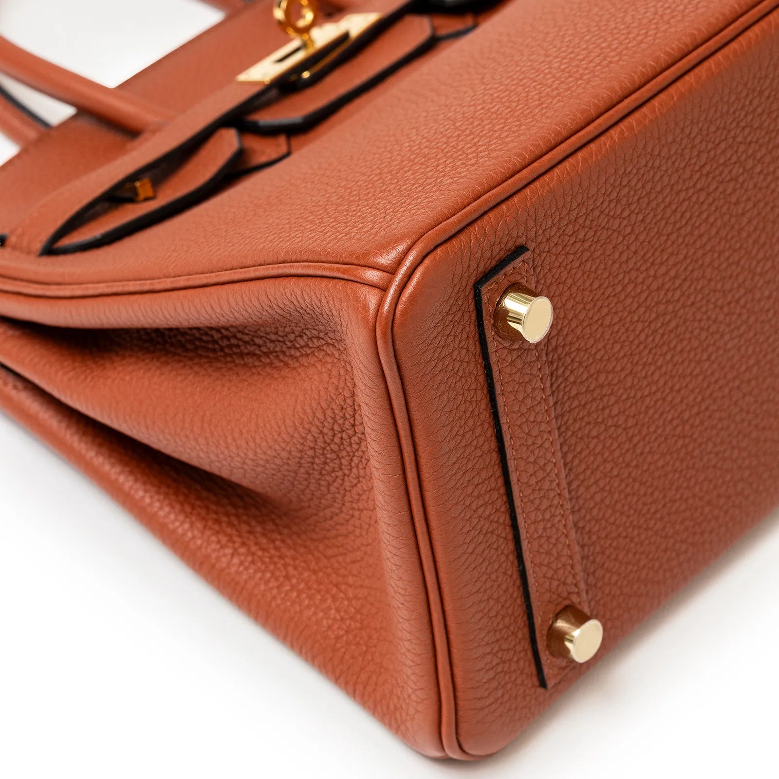Close-up of bottom corner showing copper togo leather texture and gold hardware feet on Hermès Birkin 25 bag