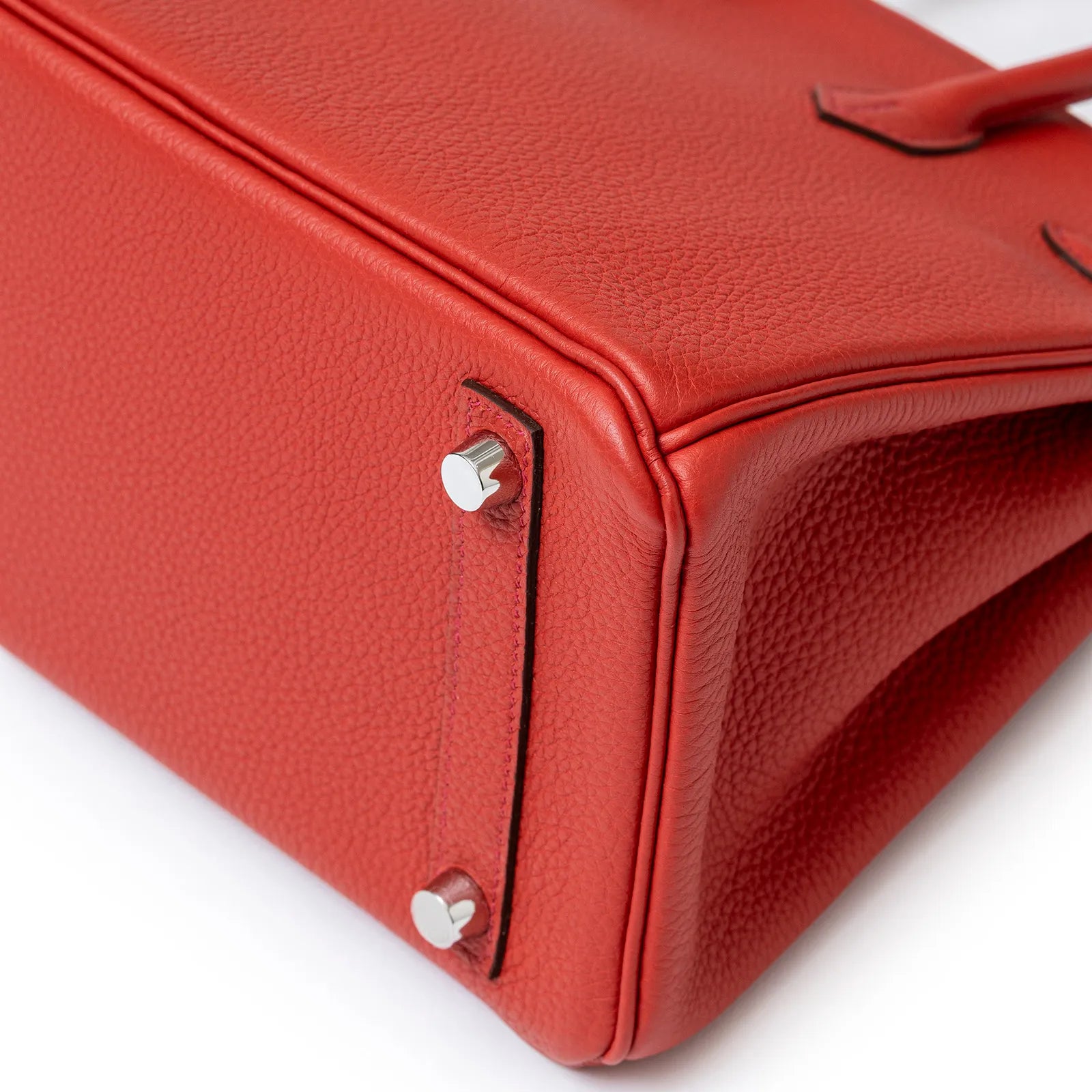 Close-up of Hermès Birkin 25 Geranium Togo Palladium Hardware showing detailed leather and metal feet on bag corner.