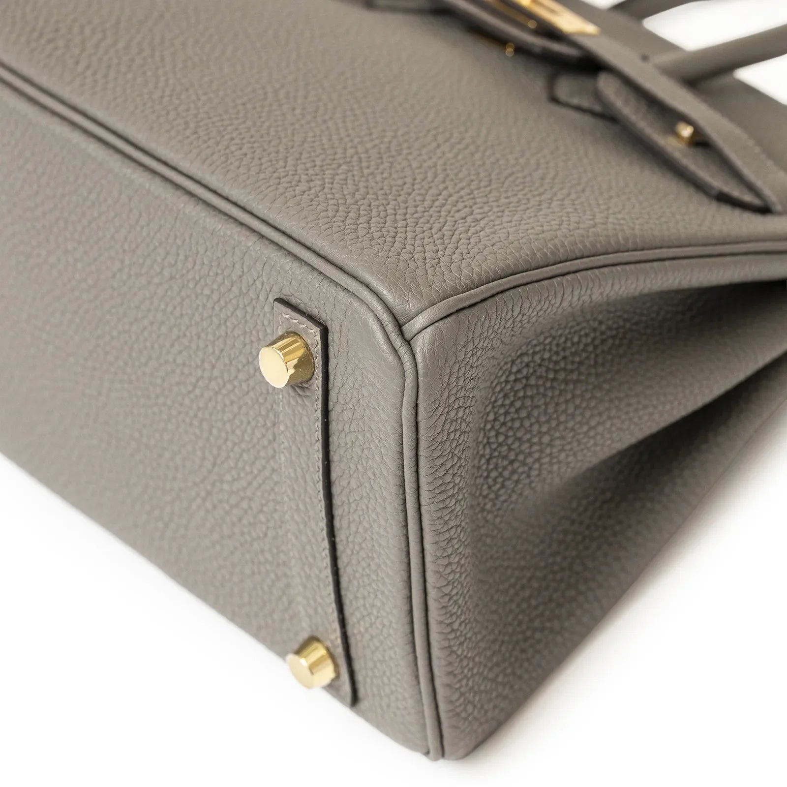 Close-up angled view of Hermès Birkin 25 Gris Meyer togo leather corner with gold hardware feet details