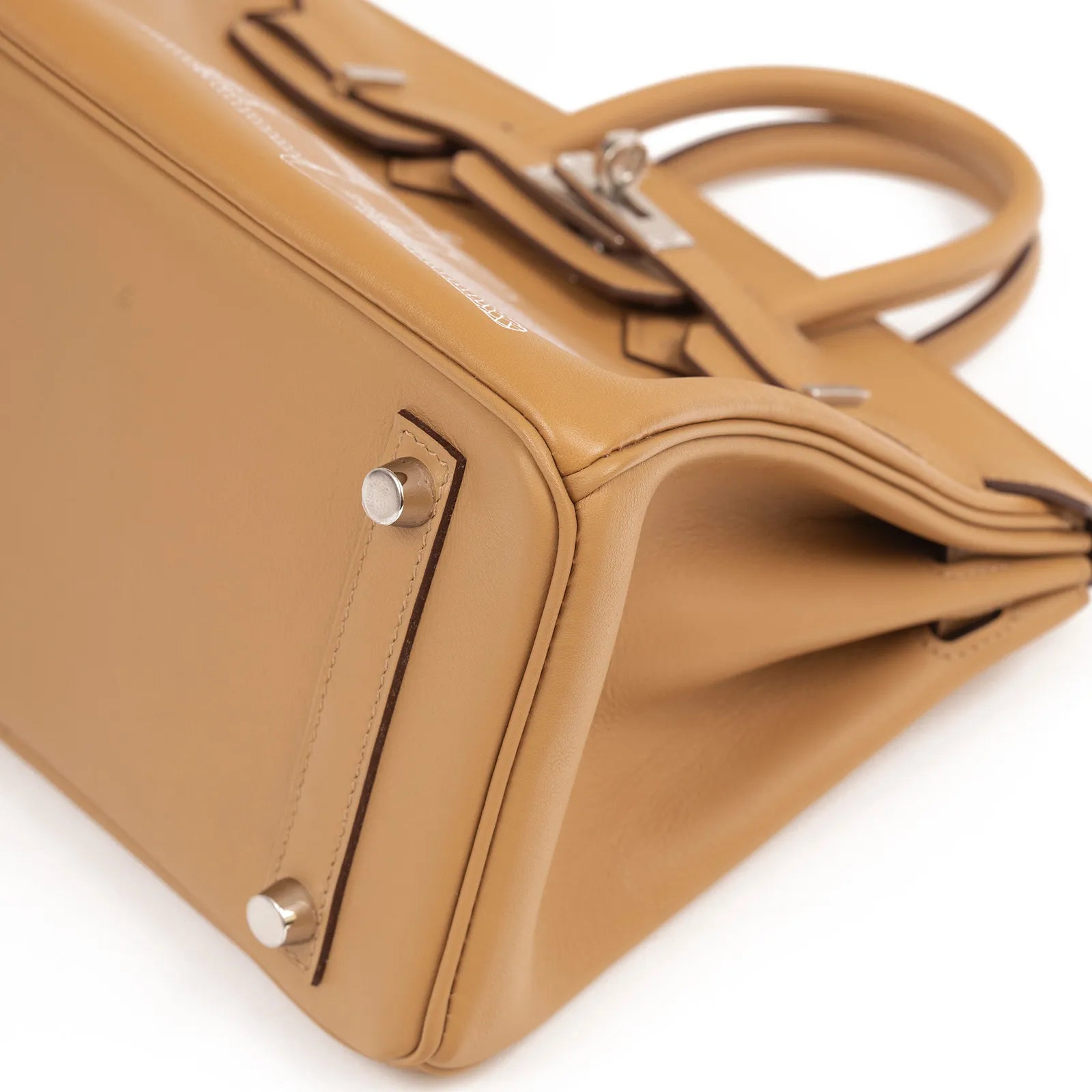 Close-up angled shot of Hermès Birkin 25 in biscuit leather showing palladium hardware and structured base feet