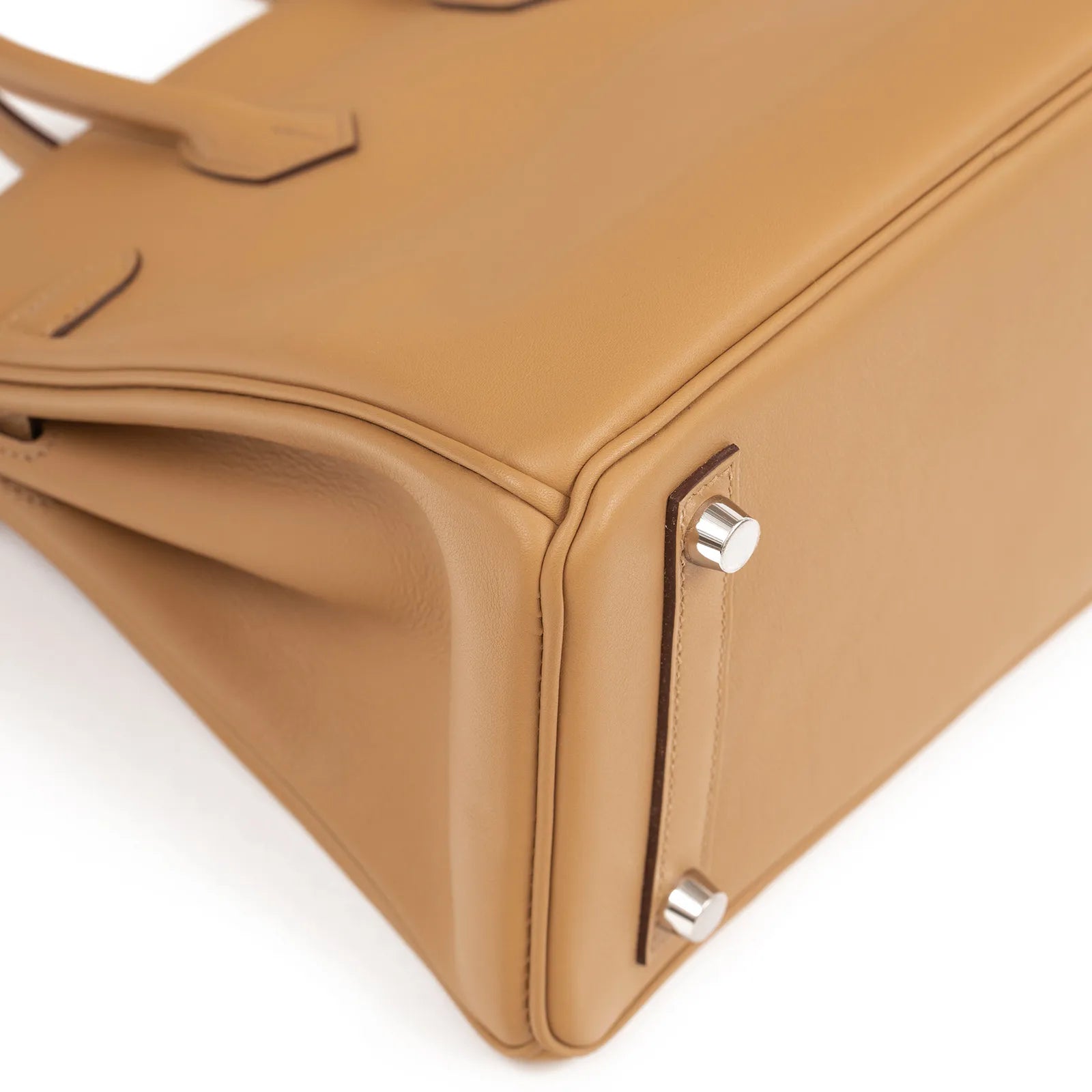 Close-up angled shot of biscuit leather base showing palladium hardware feet and clean corner stitching detail