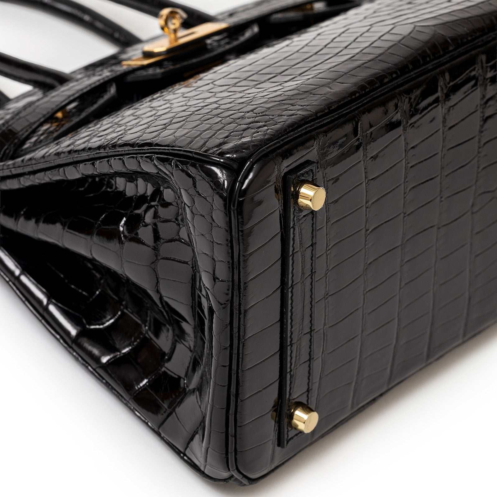 Close-up of bottom corner showing black shiny Porosus crocodile and gold hardware on Hermès Birkin 30