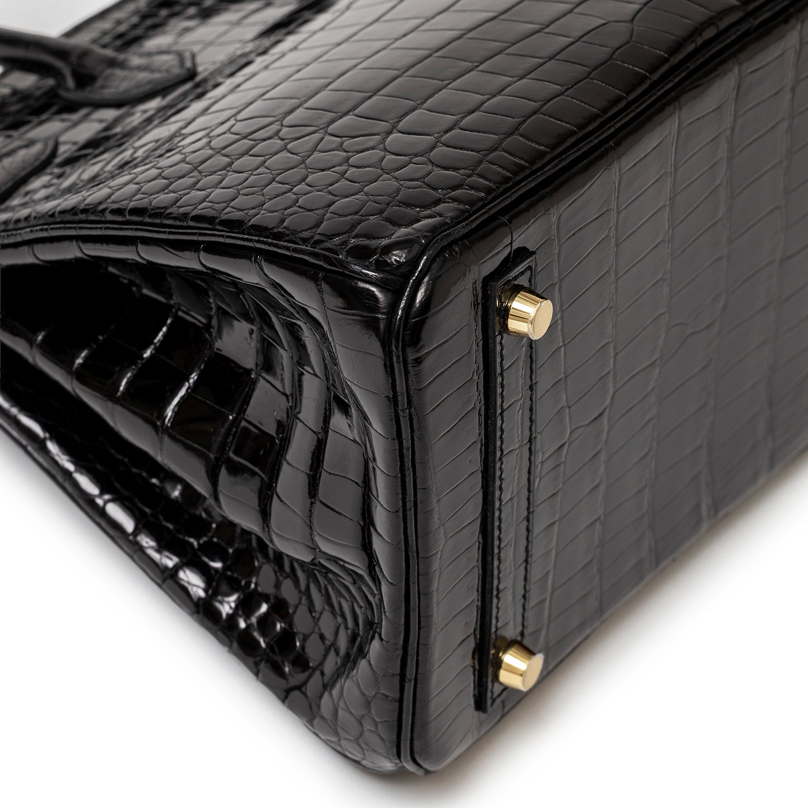 Close-up of bottom corner of Hermès Birkin 30 Black Shiny Porosus Crocodile with gold hardware feet.