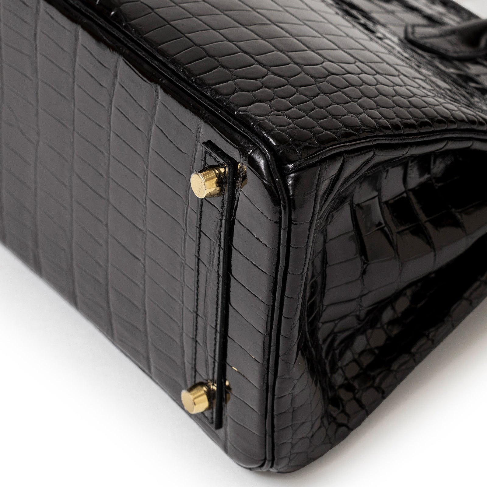 Close-up angled shot of Hermès Birkin 30 Black Shiny Porosus Crocodile with gold hardware feet detail