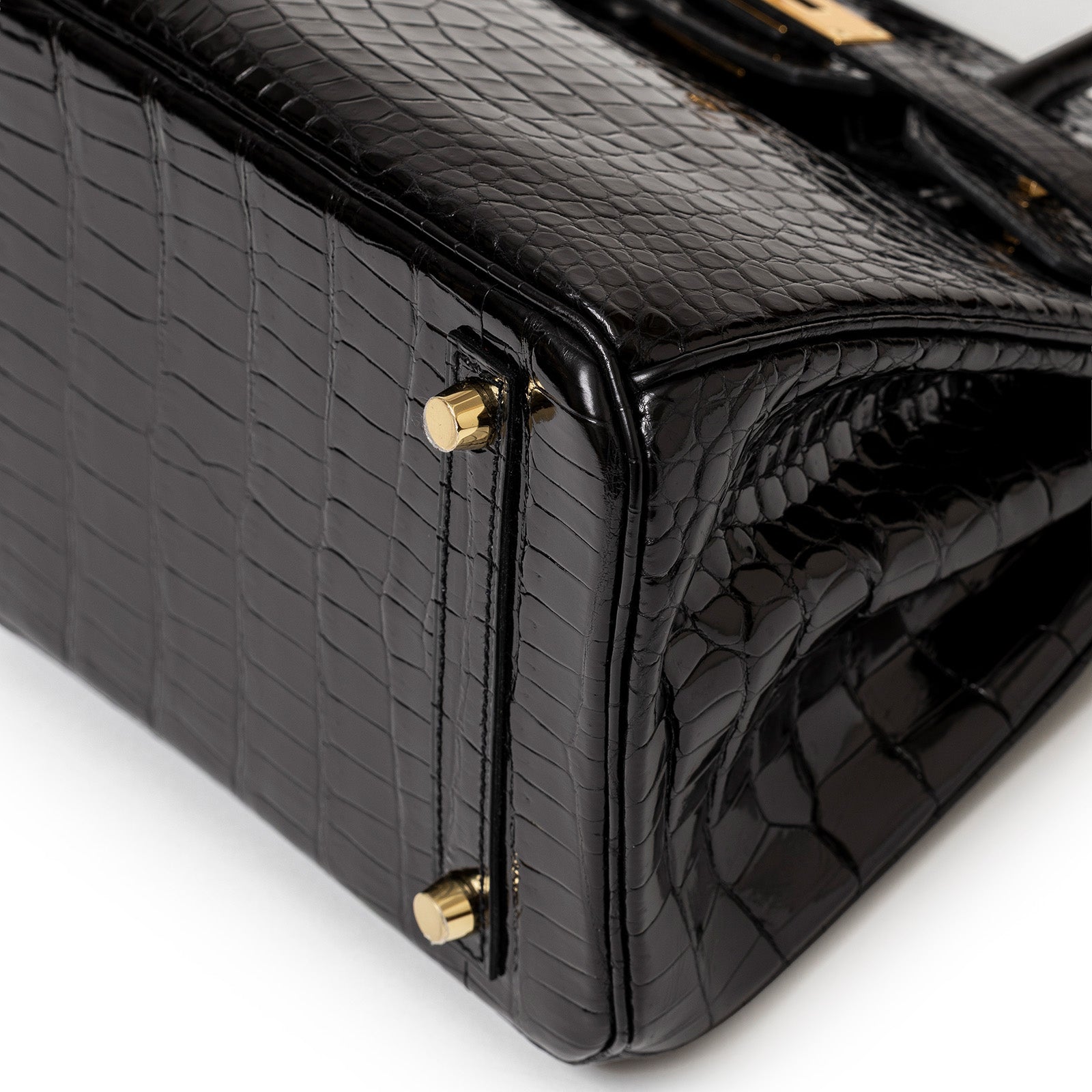Close-up of bottom corner showing gold hardware and shiny black Porosus crocodile texture on Hermès Birkin 30