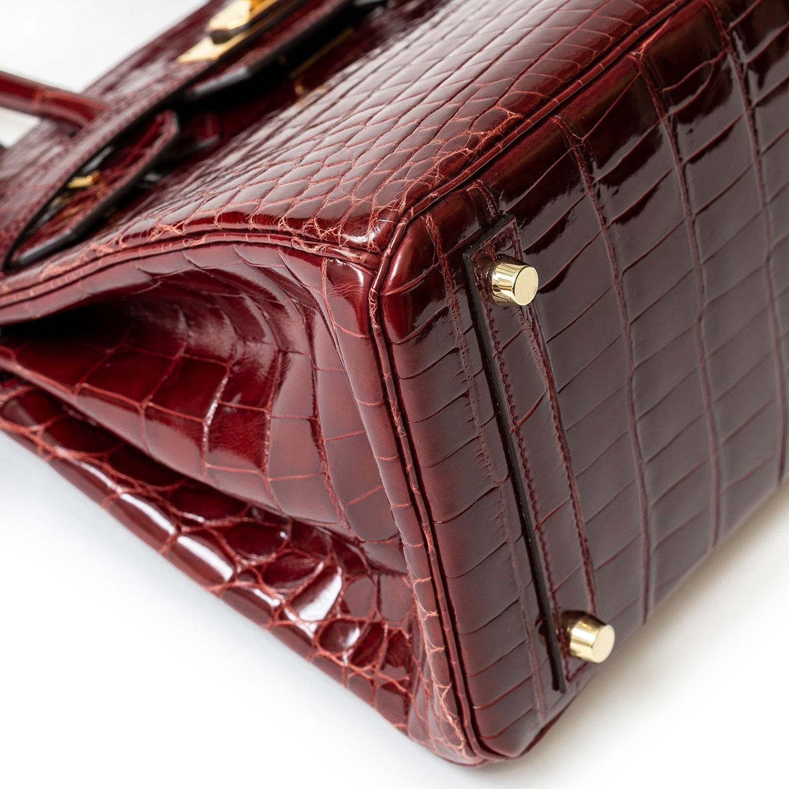 Close-up of bottom corner showing shiny burgundy Niloticus crocodile texture and gold hardware feet.