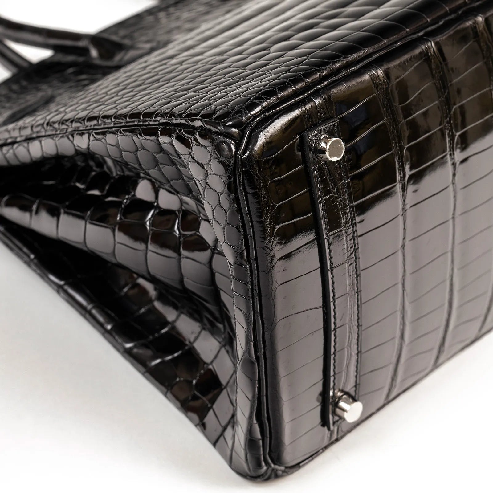 Close-up of Hermès Birkin 35 Black Shiny Porosus showing textured leather and palladium hardware feet.