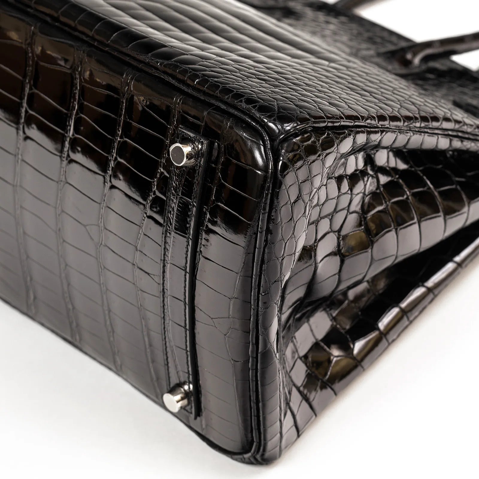 Close-up of bottom corner showing black shiny Porosus leather and palladium hardware on Hermès Birkin 35