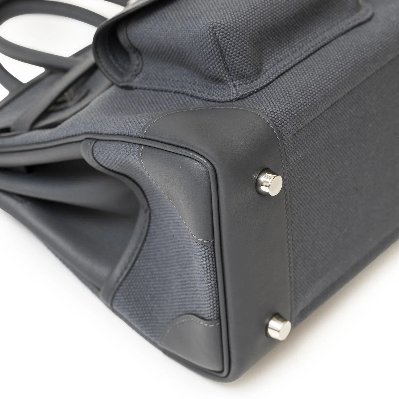 Close-up angled view of bottom corner showing dark canvas, black leather trim, and palladium feet hardware.