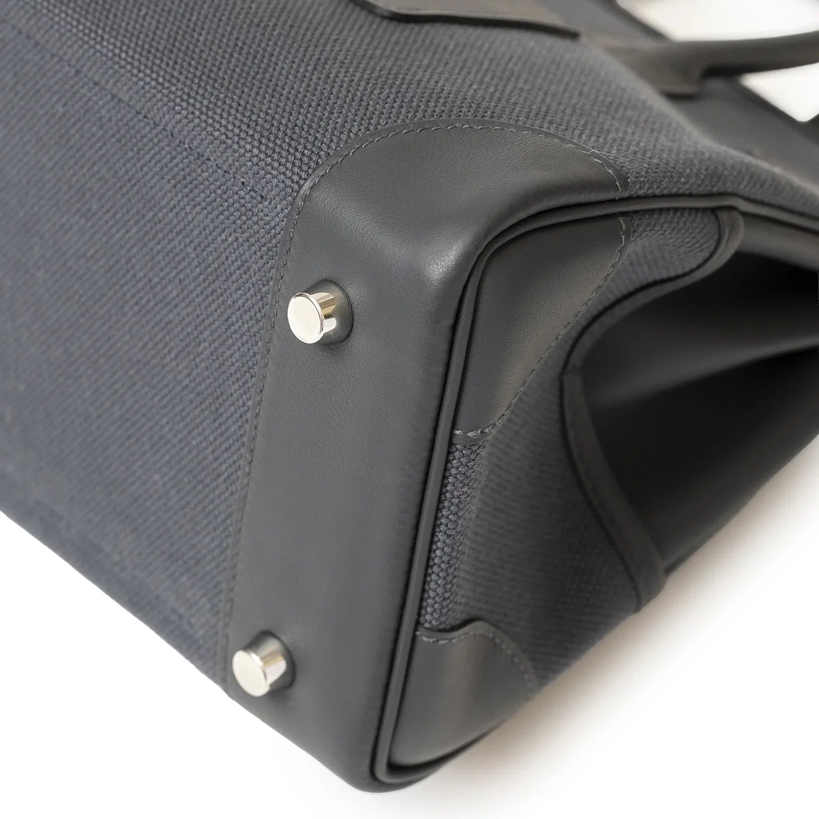 Close-up of bag corner showing textured canvas body with smooth leather trim and palladium hardware feet