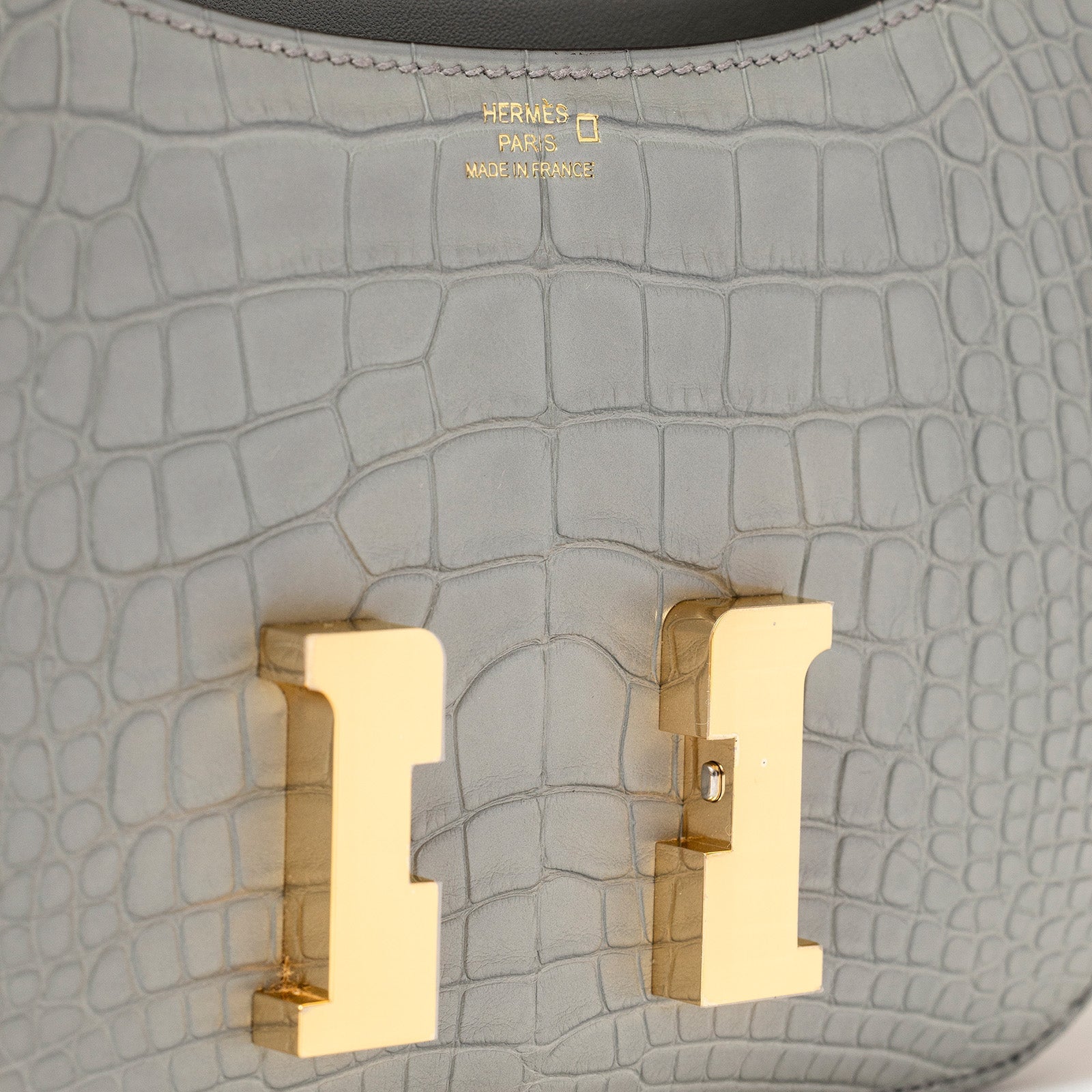 Close-up of gold hardware clasp on Hermès Mini Constance 18 Gris Ciment Matte Alligator handbag