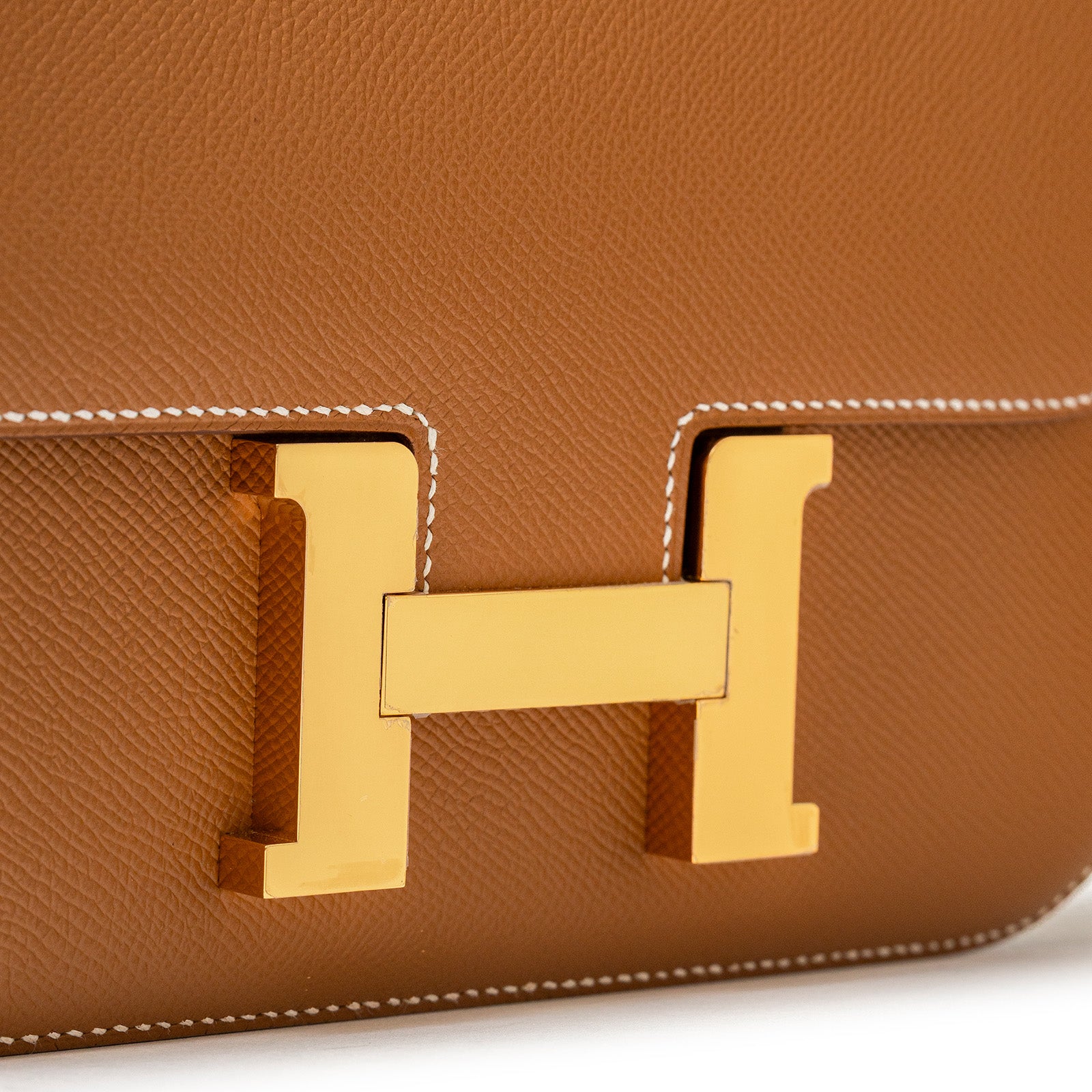 Close-up of Hermès Constance 24 Gold Epsom Gold Hardware showcasing gold clasp on tan leather with white stitching