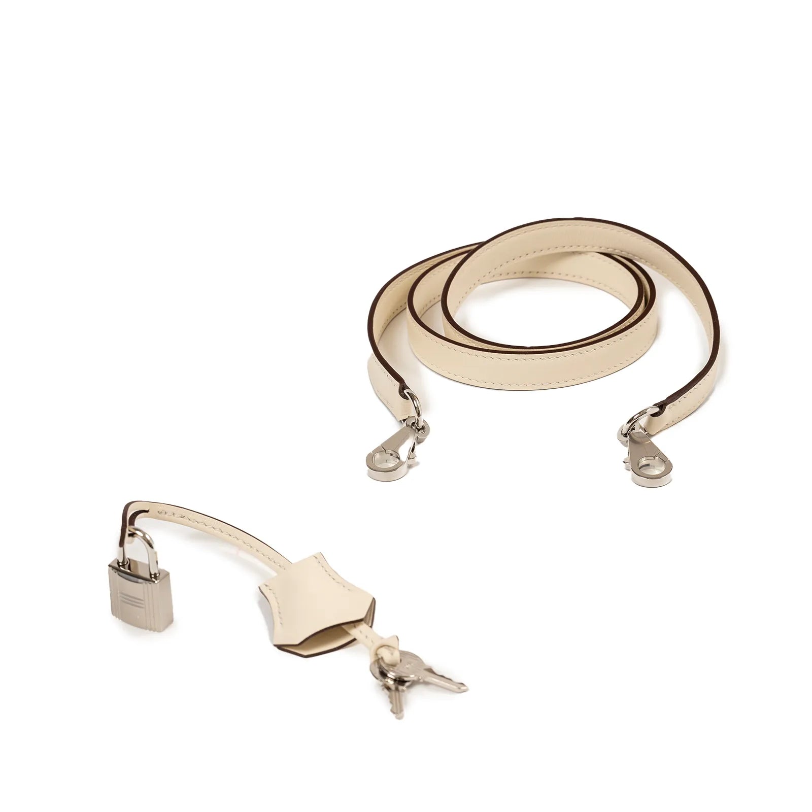 Top-down view of cream leather Hermès strap with palladium hardware, lock, and two keys on white background