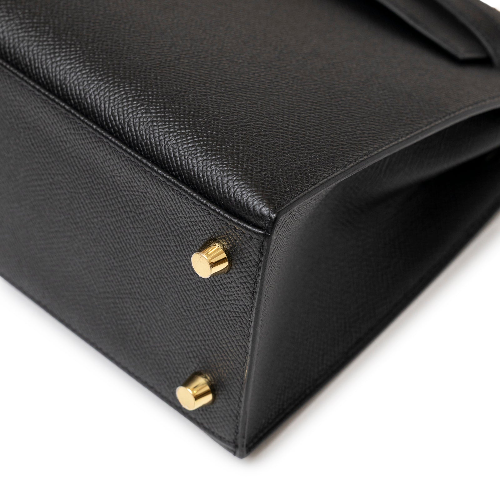 Close-up of black textured leather corner with gold hardware feet on Hermès Kelly 25 Sellier Black Epsom Gold hardware bag