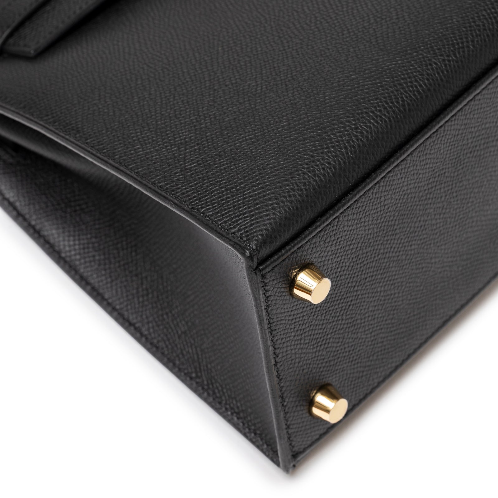 Close-up of bottom corner showing textured black Epsom leather and gold feet on Hermès Kelly 25 Sellier Black Epsom Gold Hardware
