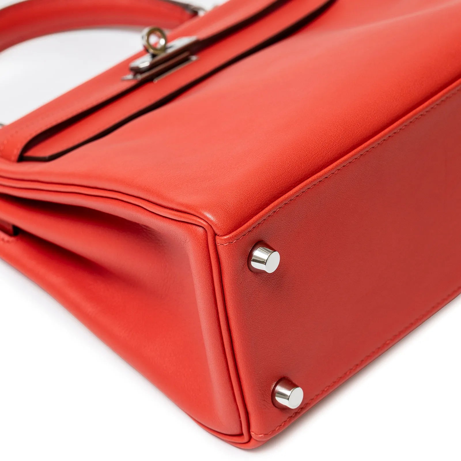 Close-up angled shot of the bottom corner of Hermès Kelly 25 Retourne Rouge Swift Palladium Hardware bag showing metal feet and leather texture