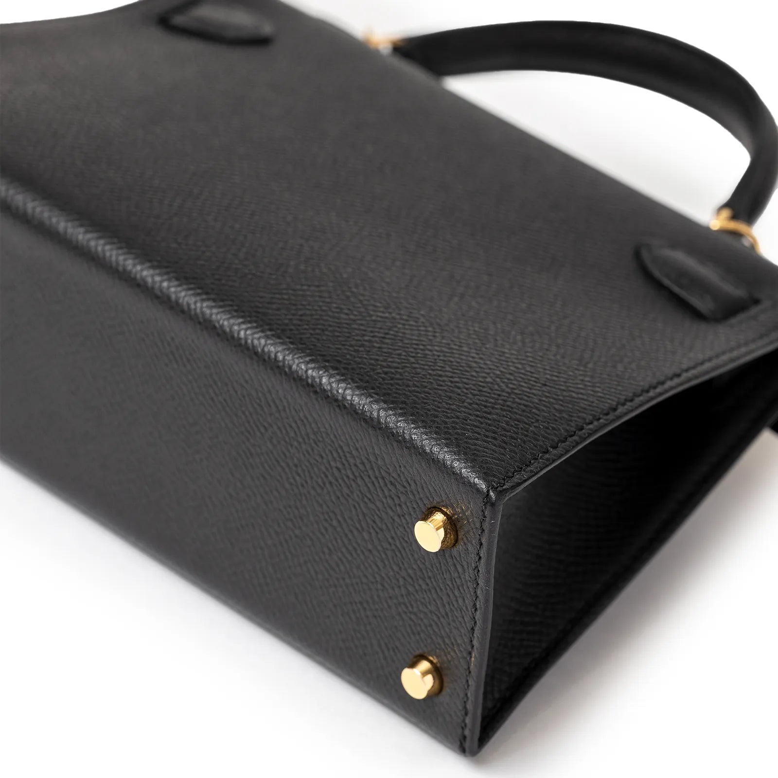 Black leather handbag angled view with gold studs and a sleek handle.