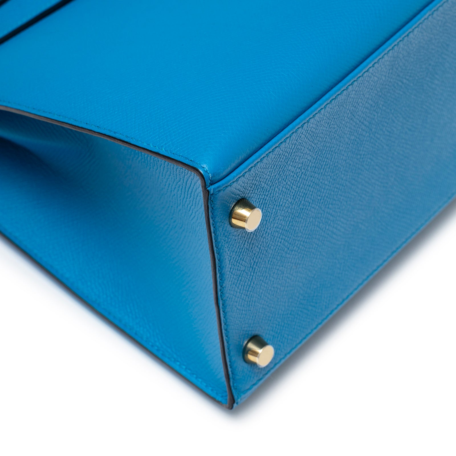 Close-up angled shot of the bottom corner of Hermès Kelly Sellier 28 Blue Zanzibar Epsom Gold Hardware highlighting gold feet and texture.
