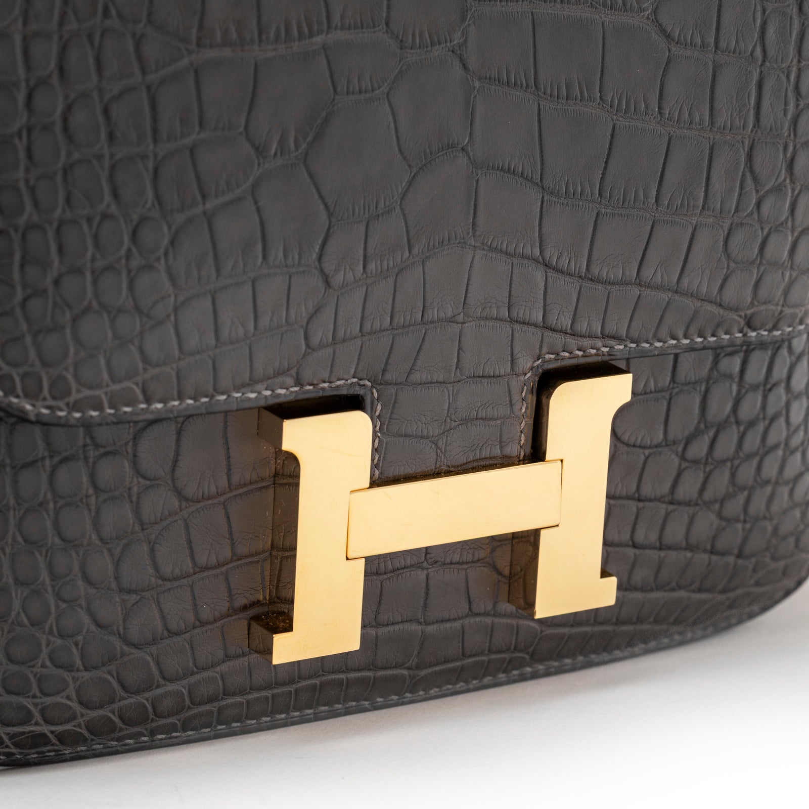 Close-up of Hermès Mini Constance 18 Graphite Matte Alligator Gold Hardware showing polished gold H clasp and textured leather