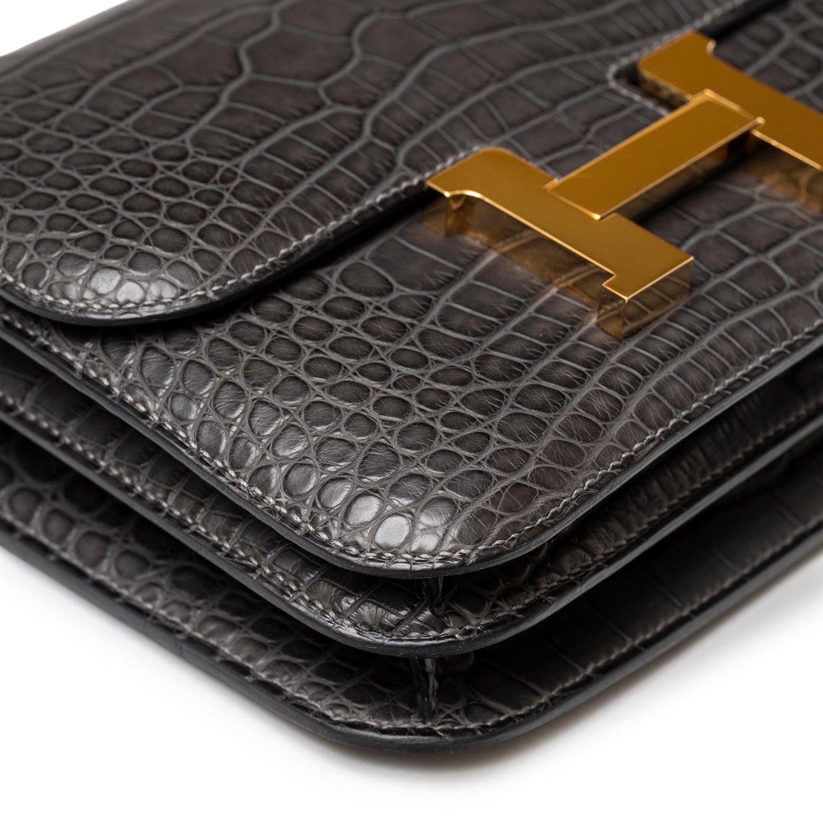 Close-up of Hermès Mini Constance 18 Graphite Matte Alligator Gold Hardware flap and polished gold H clasp detail