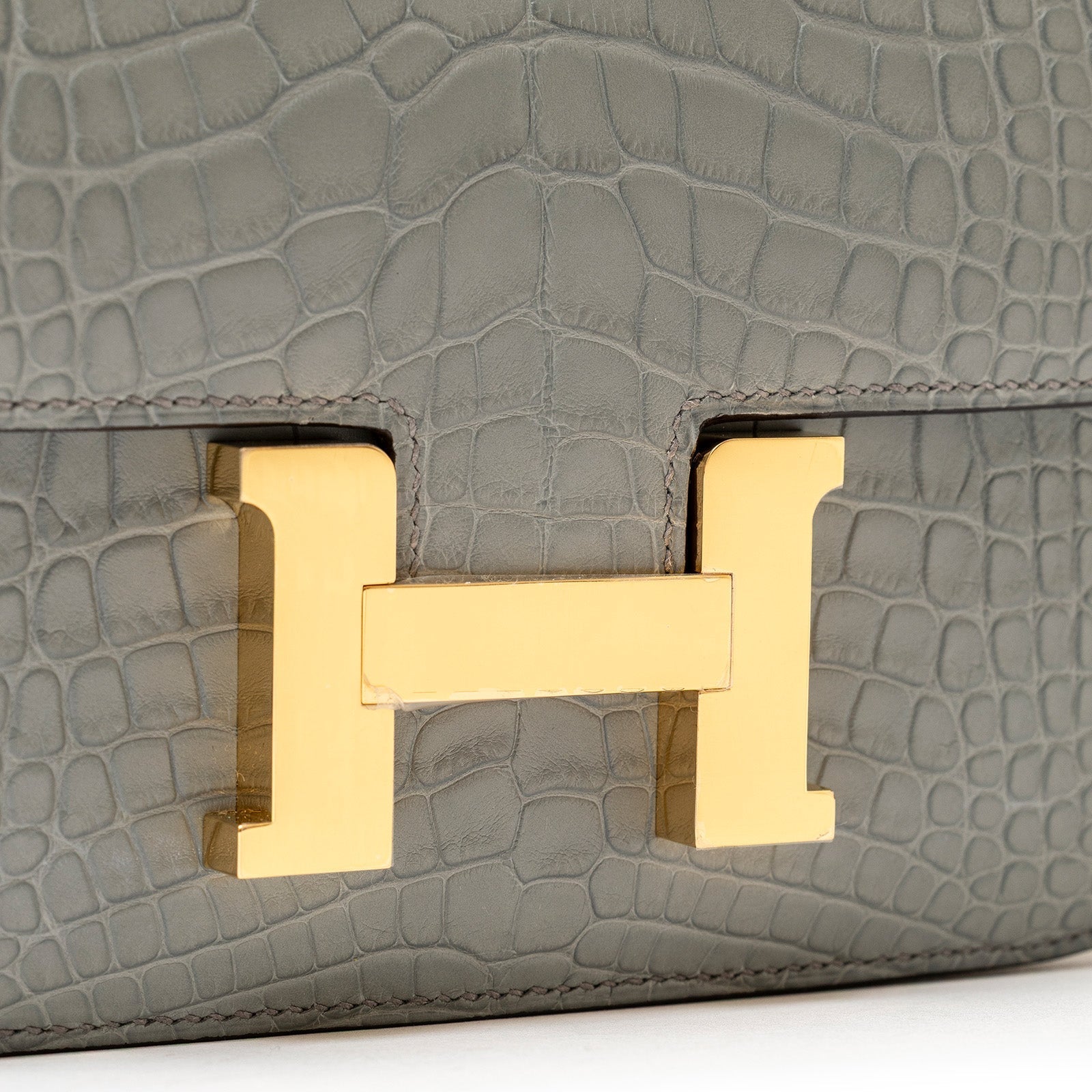 Close-up front view of Hermès Mini Constance 18 Gris Ciment Matte Alligator Gold Hardware clasp detail